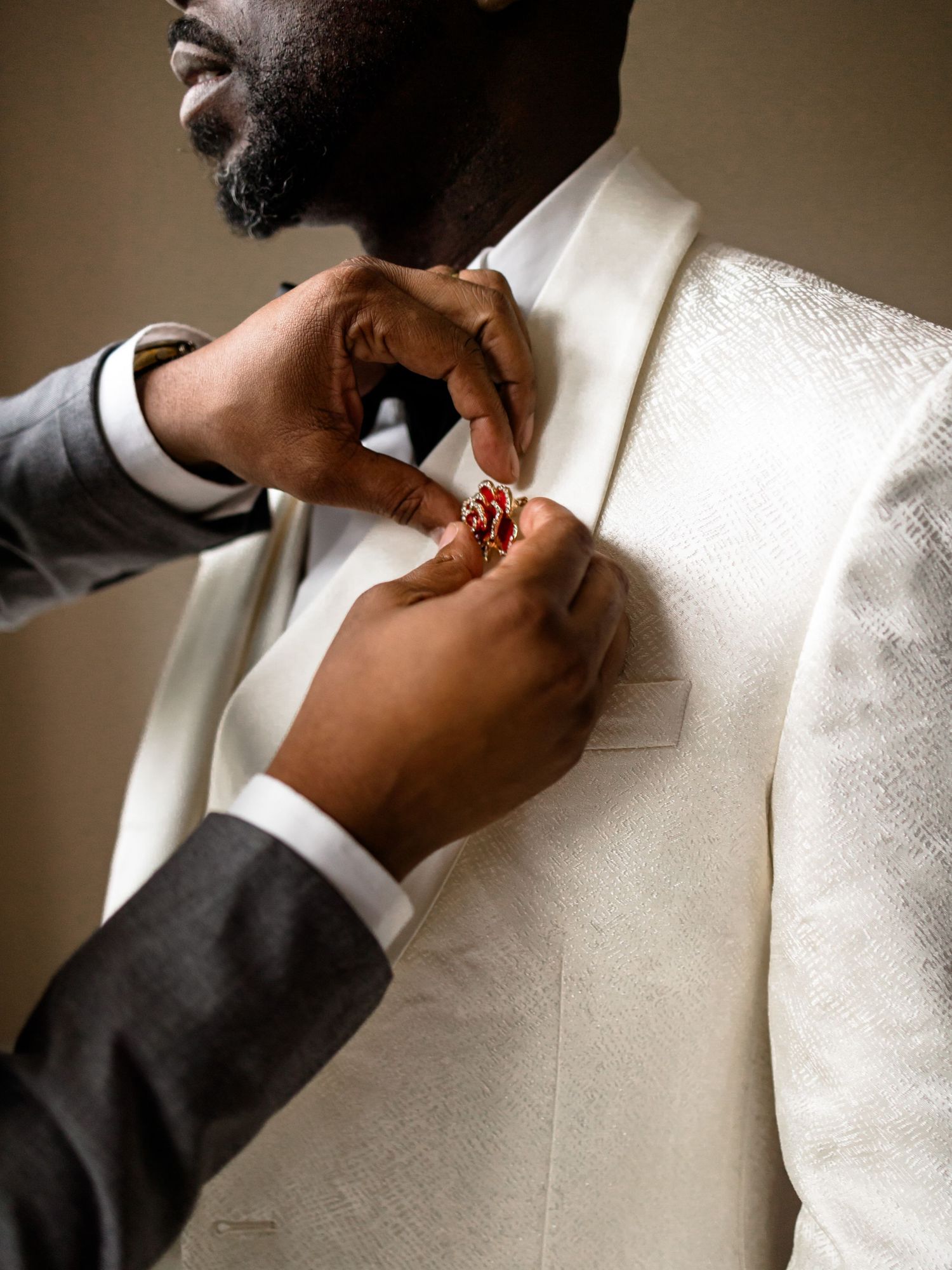 Close-up shots of hands adjusting a formal white suit jacket and boutonniere.
