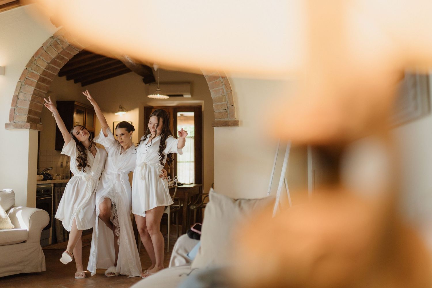 Bridesmaids in white robes celebrating together in a rustic Tuscan villa with arched brick doorways.