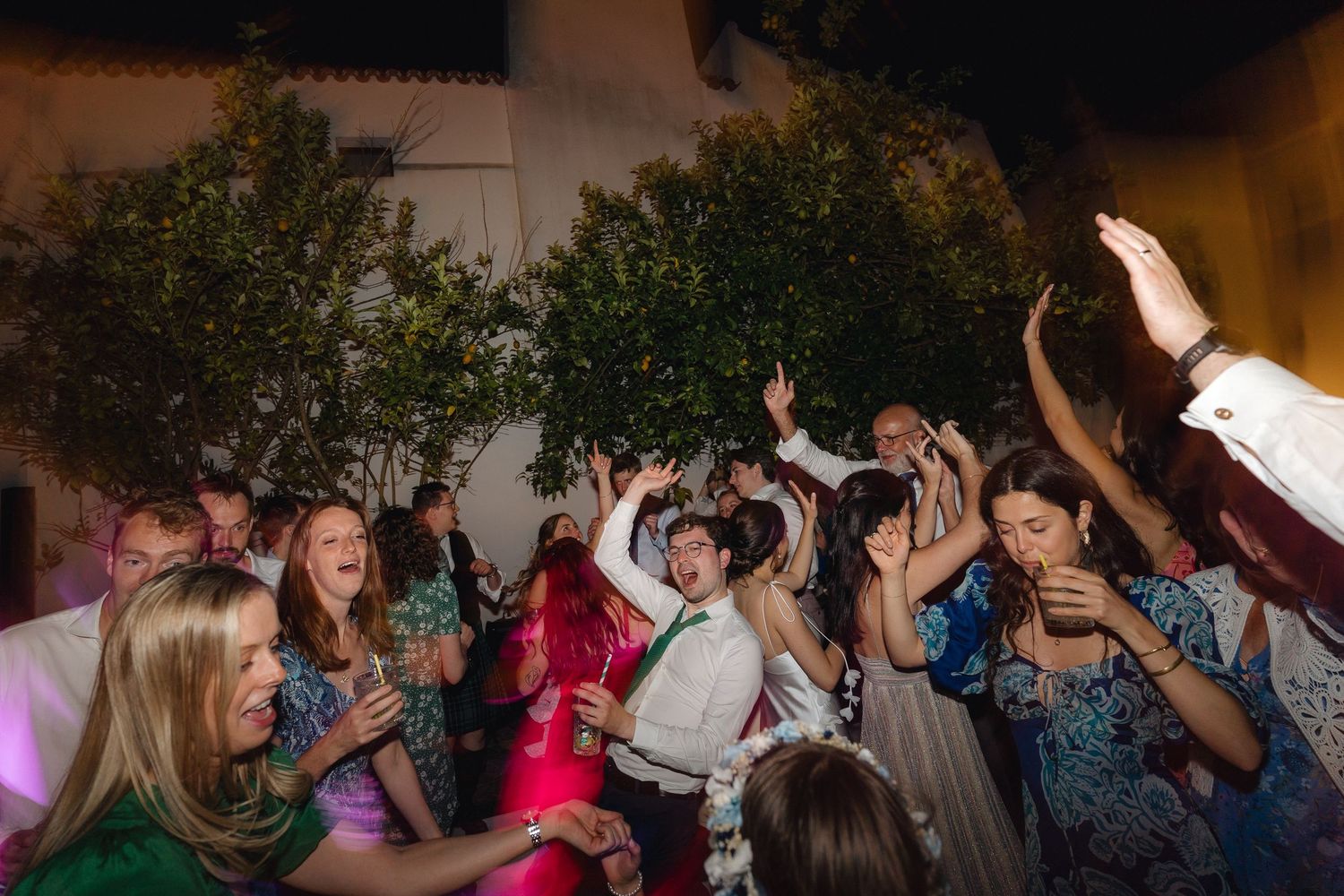 Crowd of party attendees dancing with hands in the air under ambient lighting.