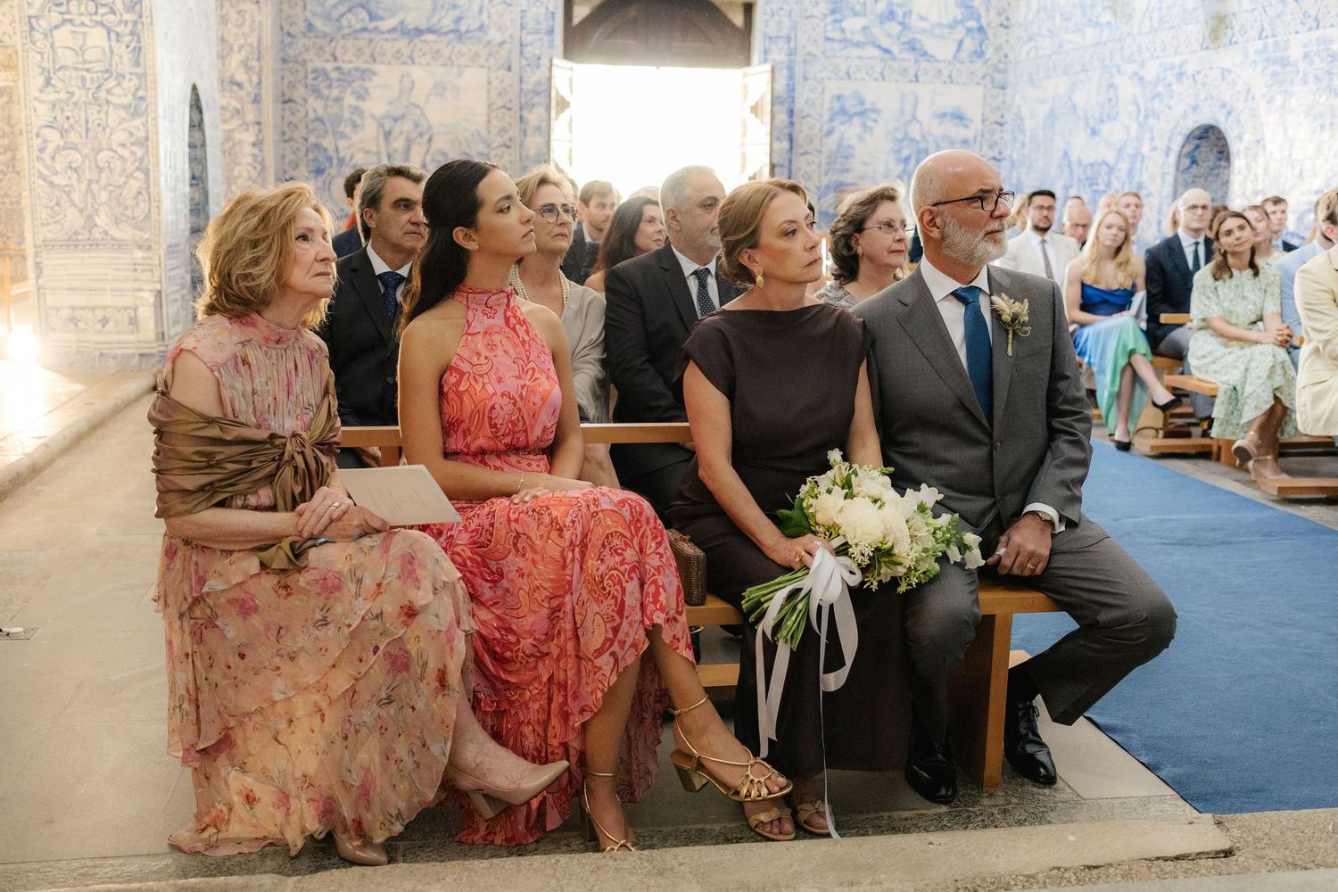 Wedding guests seated in church pews with traditional Portuguese blue tile walls in background.
