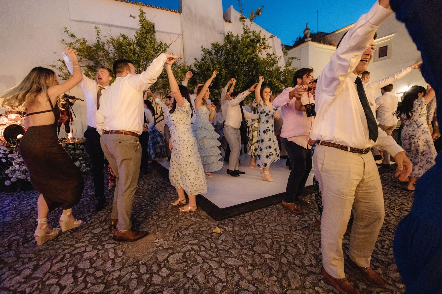 Wedding guests dancing and celebrating on a rustic cobblestone courtyard.