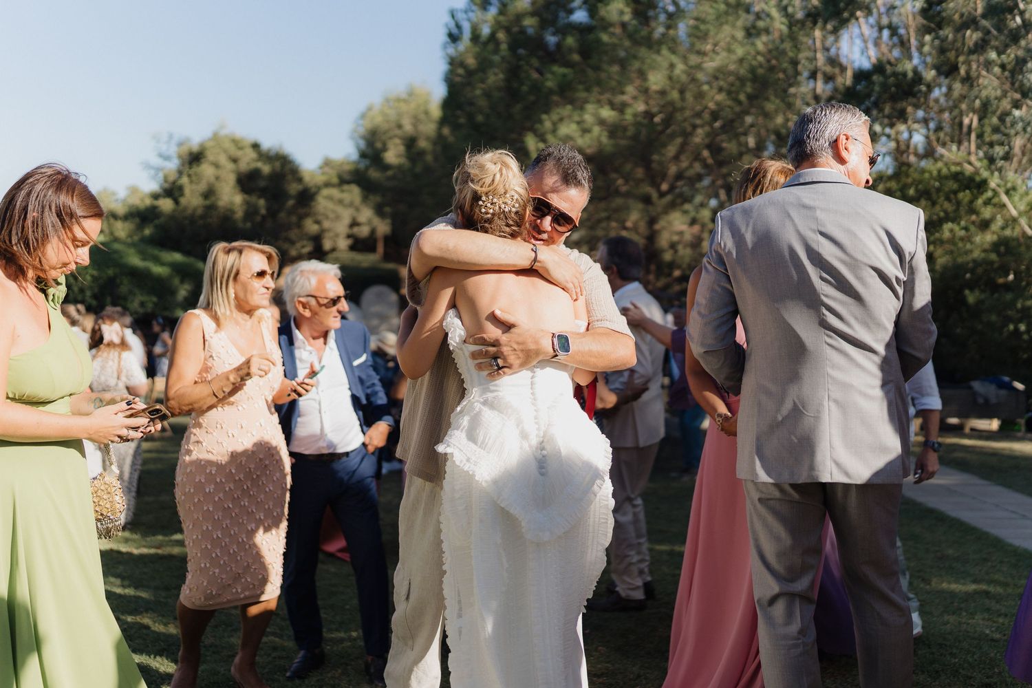 Guests mingling at an outdoor wedding reception with trees in the background.
