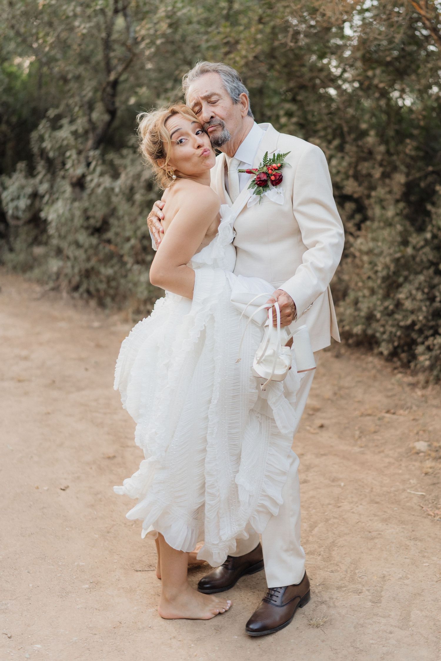 Wedding couple in white attire sharing playful moment on dirt path.