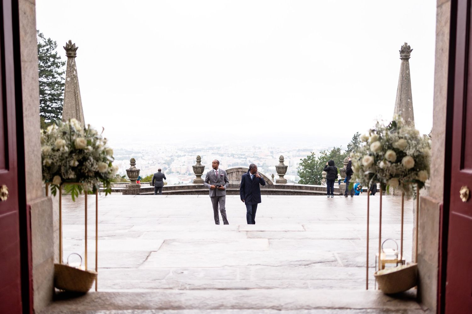 Elegant stone archway entrance with people visible in the distance at a scenic outdoor location.