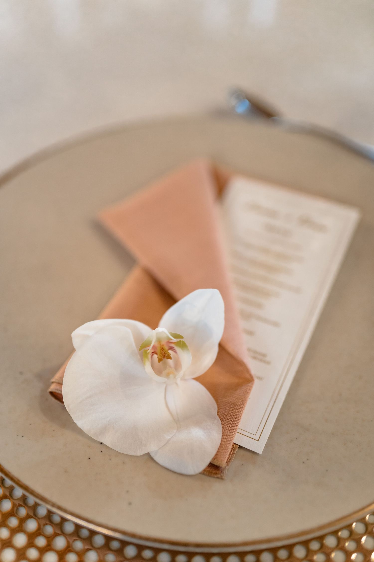Elegant place setting with a white orchid and menu card on a peach napkin.