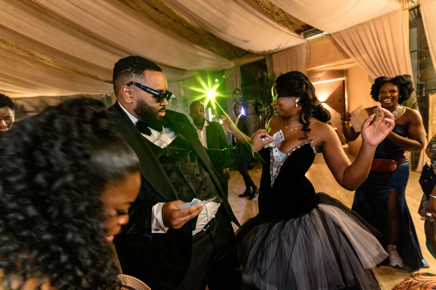 Wedding reception guests dancing and celebrating under elegant tent lighting.