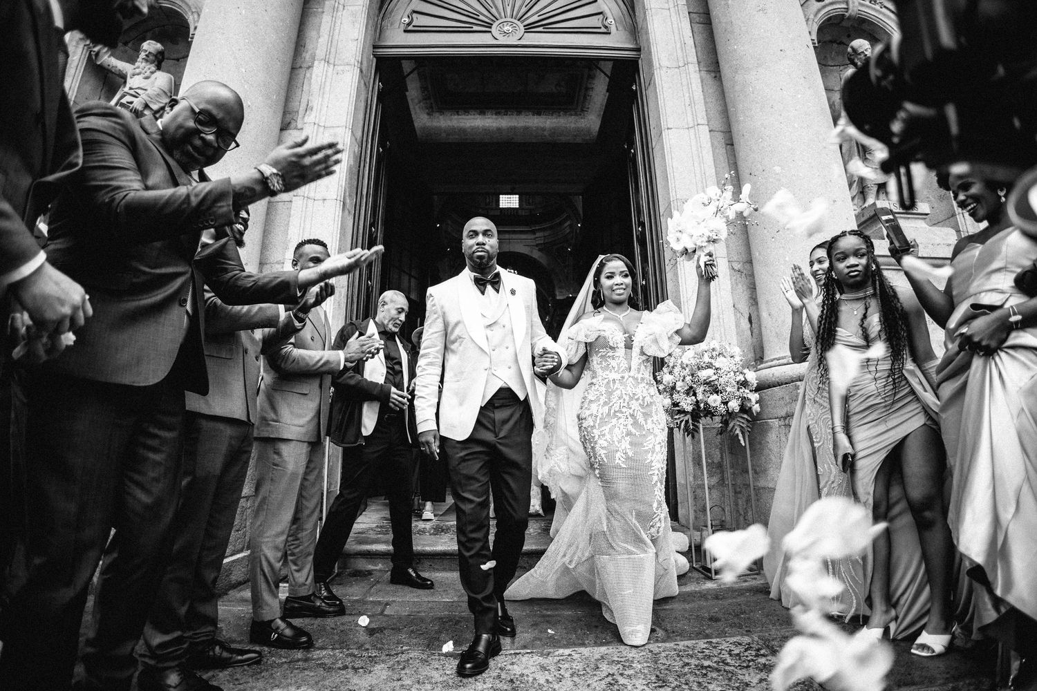 Black and white photo of newlyweds exiting church while guests celebrate.