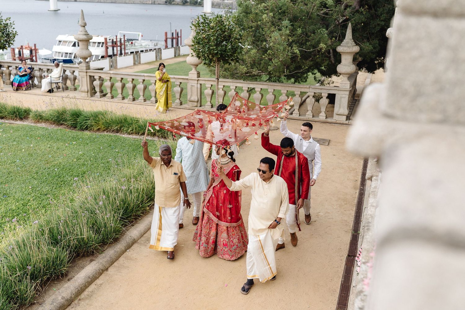 Wedding party walking along waterfront path with traditional Indian wedding attire.