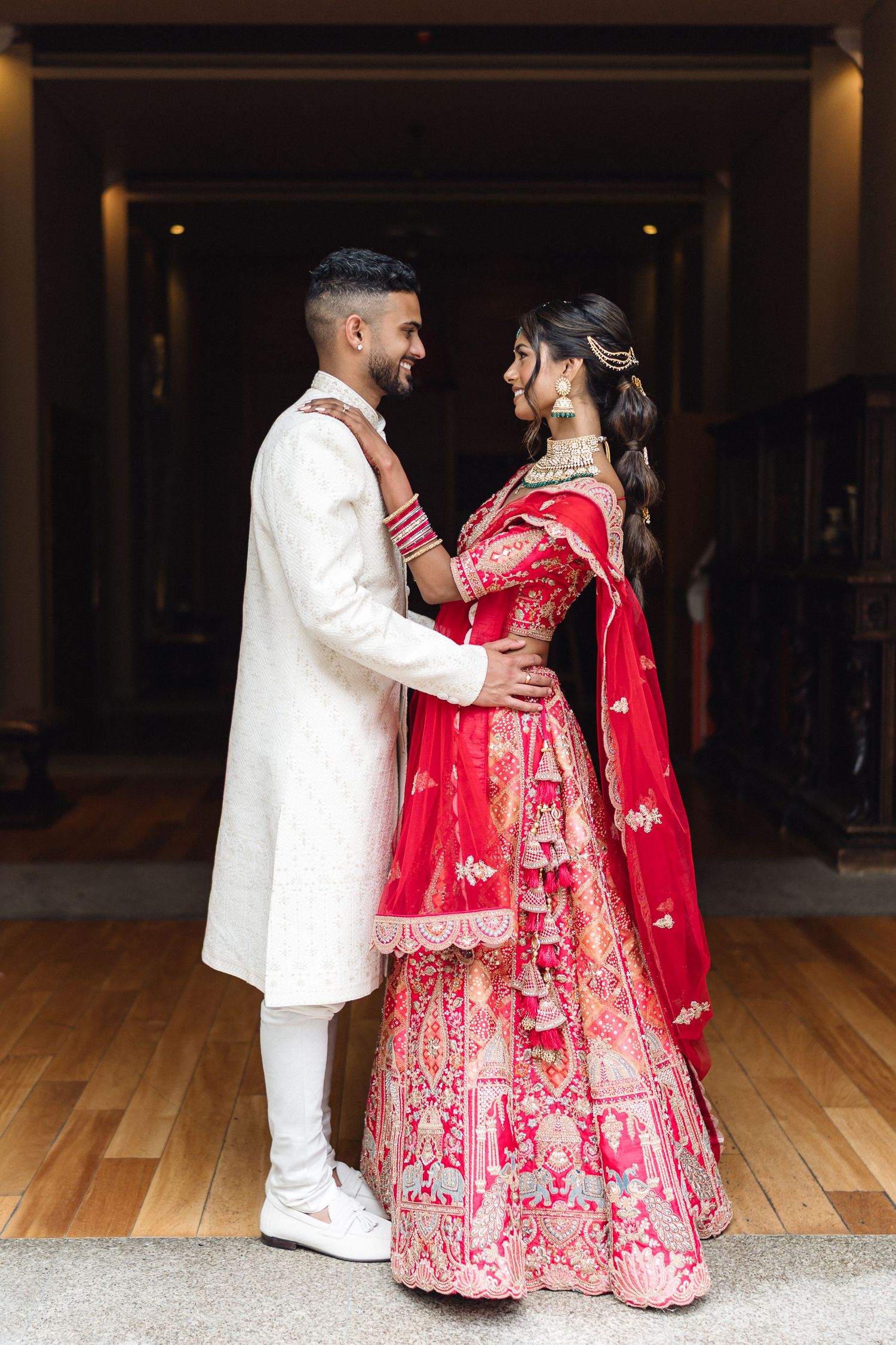 Couple in traditional Indian wedding attire dancing in an elegant indoor setting.