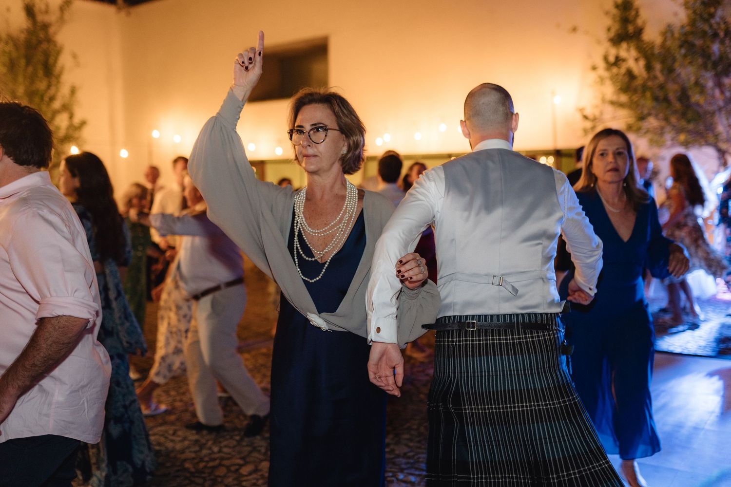 Guests dancing energetically at a wedding reception with warm ambient lighting.