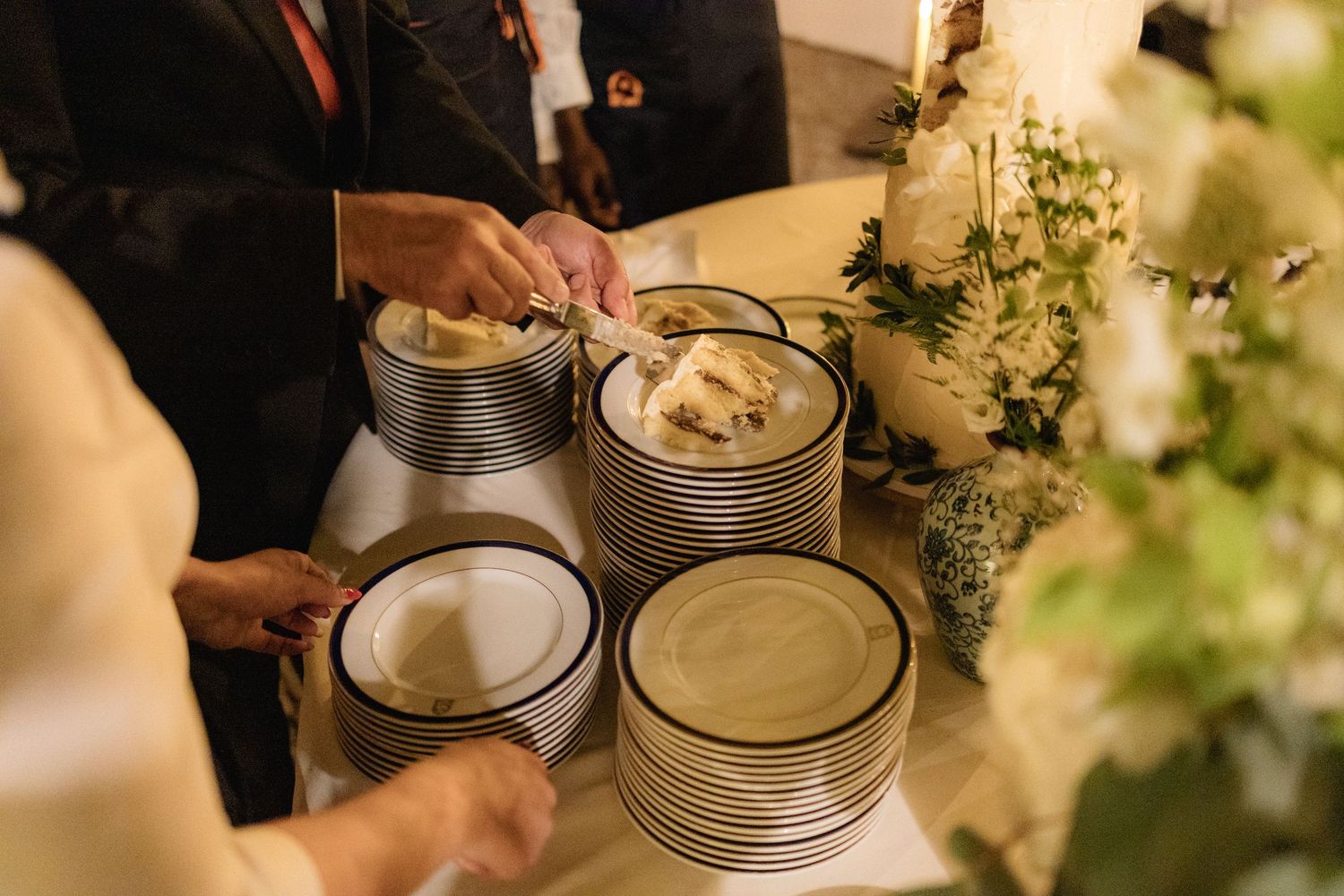 Close-up of wedding cake and place settings being prepared for service.