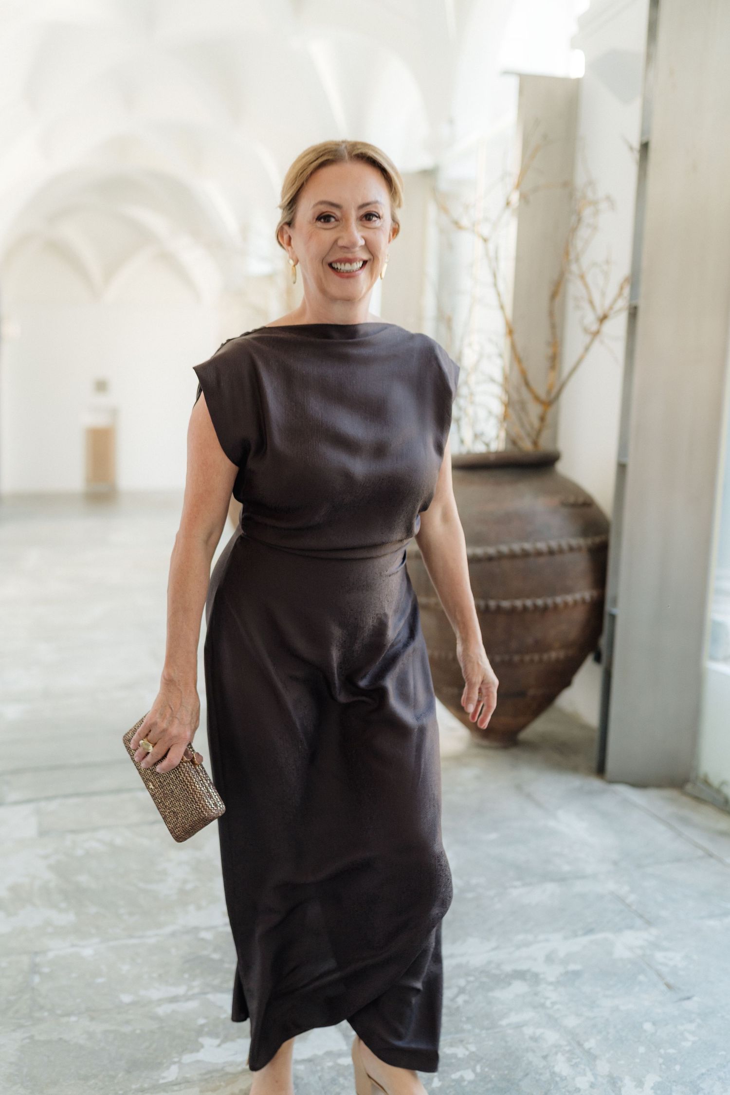 Woman in a black dress walking through a bright white hallway.