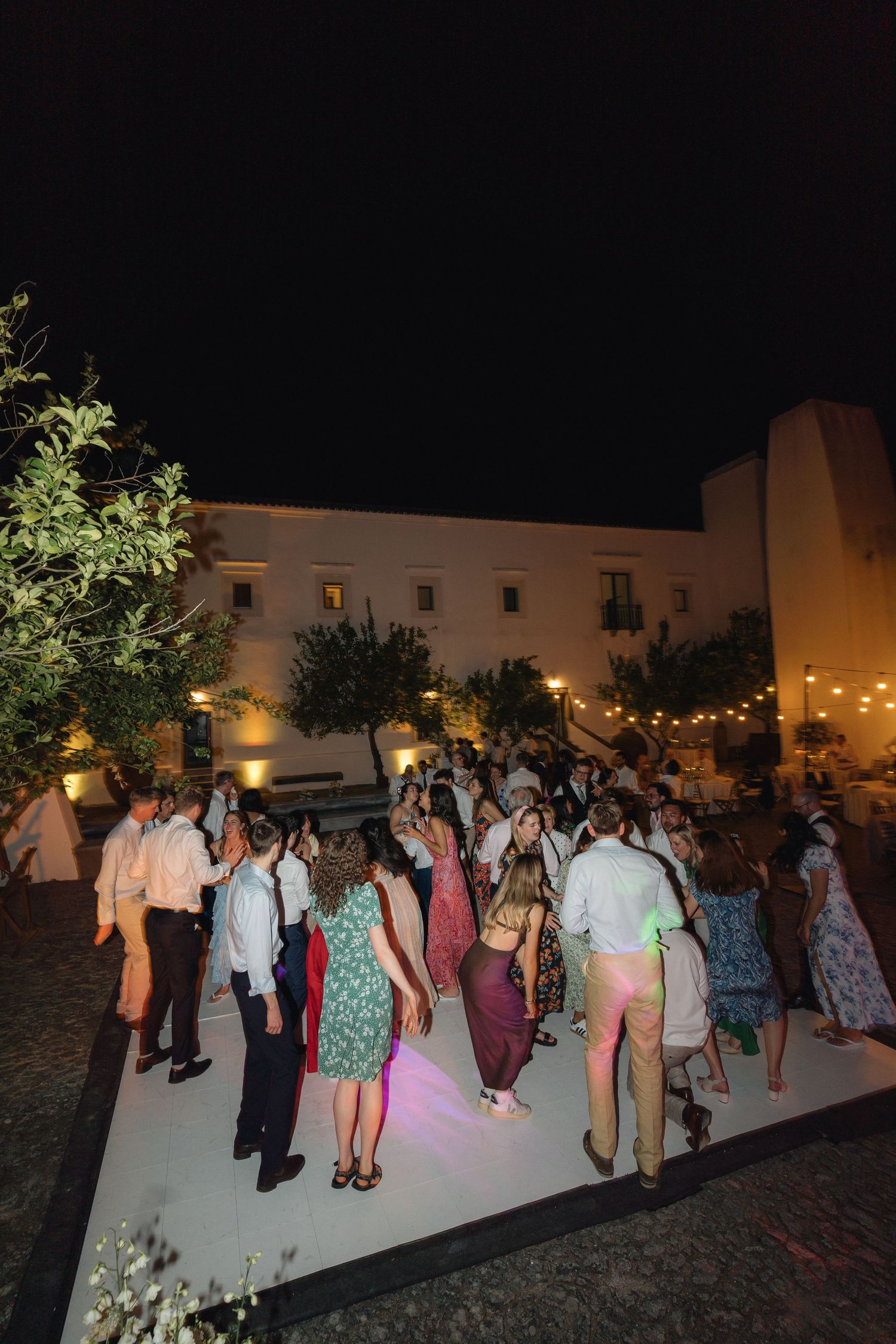 Outdoor wedding reception with guests dancing on an illuminated white dance floor.