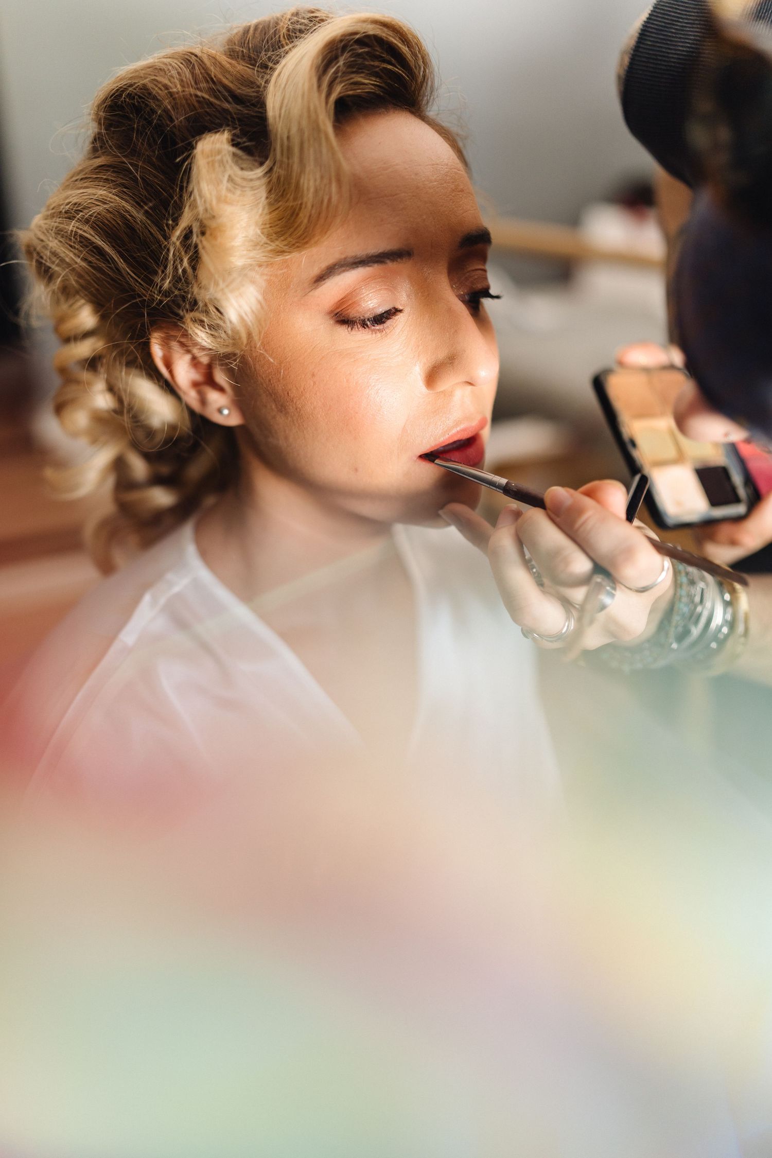 Professional makeup application in progress with soft focus and natural lighting.