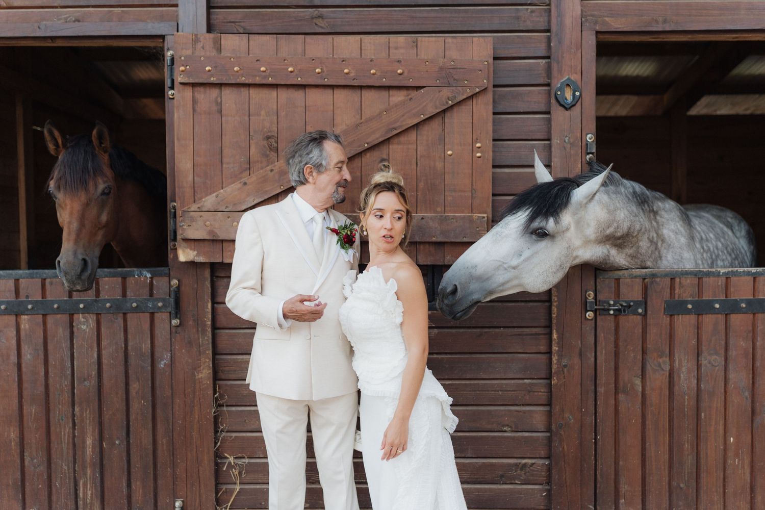 A couple in white wedding attire poses together at a rustic wooden barn venue.