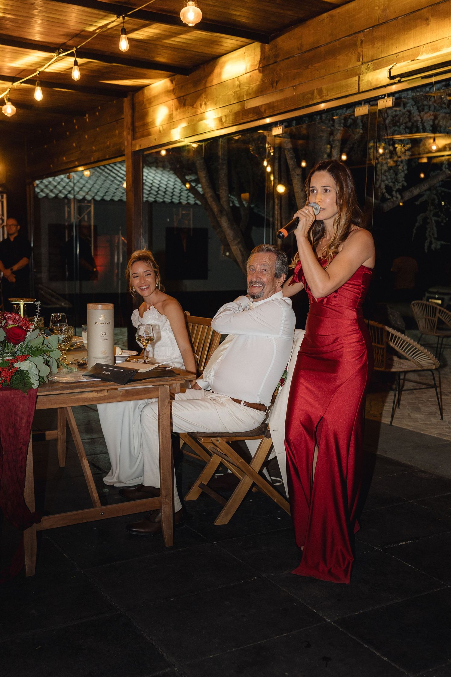 Wedding reception guests seated at wooden tables with red and white decor.