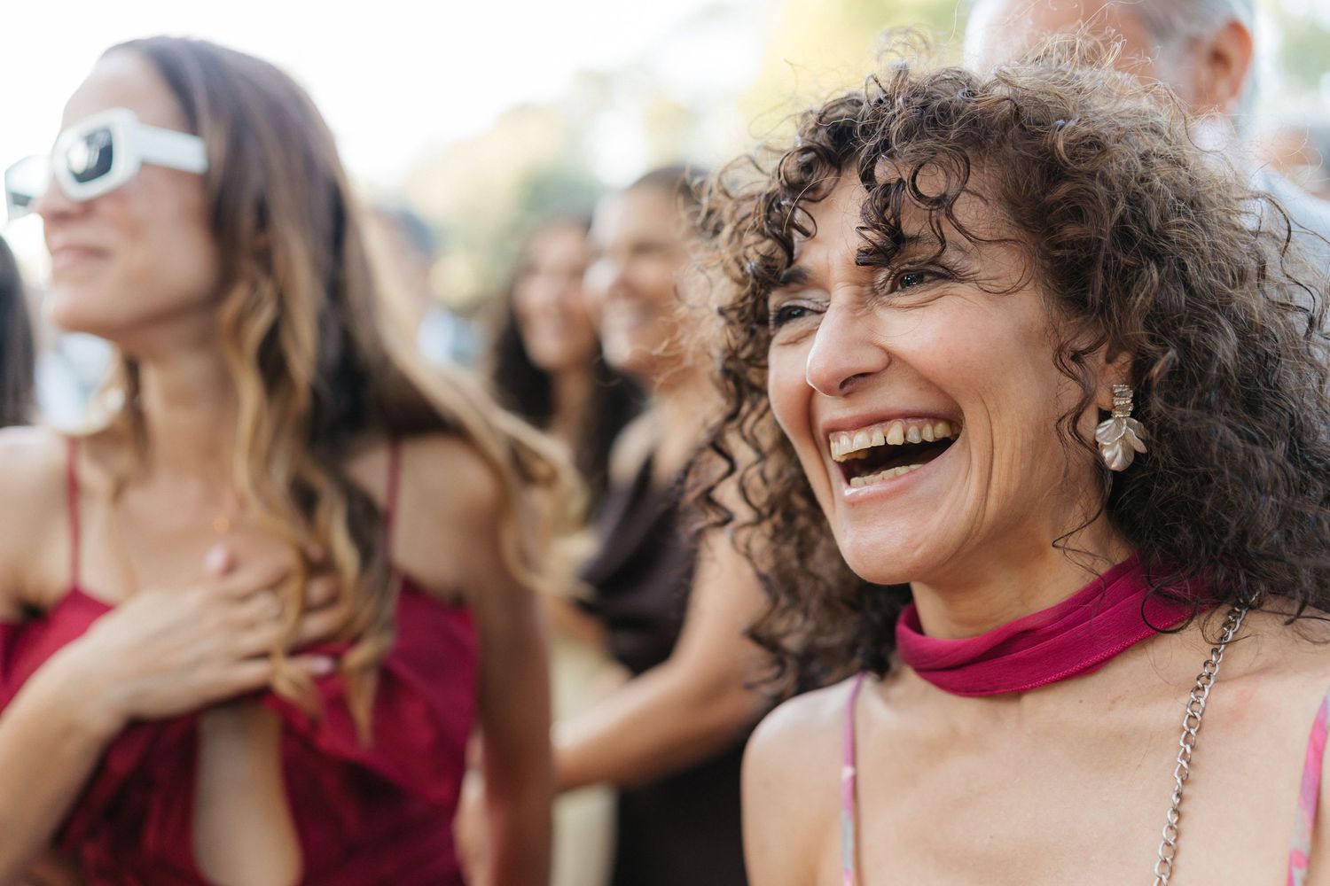 Wedding guests dancing and smiling during outdoor celebration with burgundy accents.