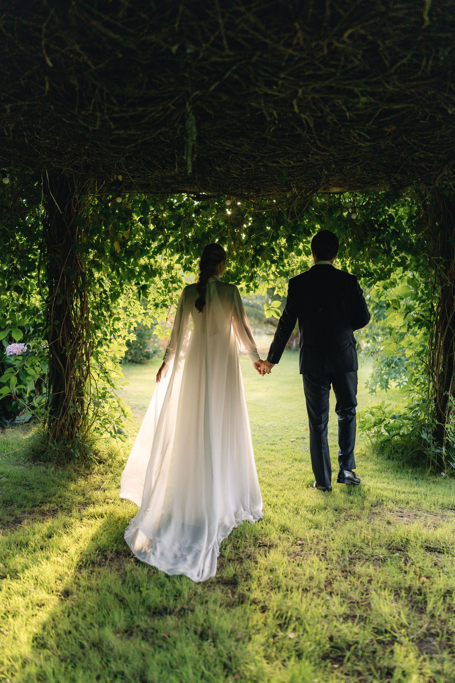 Silhouettes of couple walking through lush garden archway at sunset.