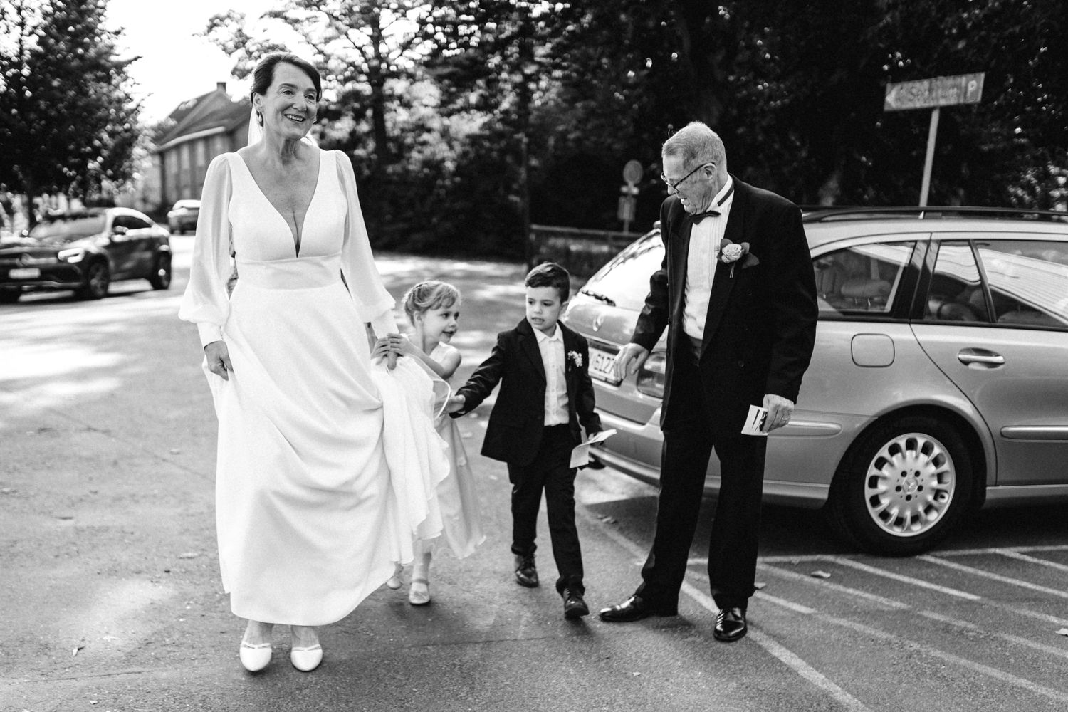 Wedding party walking together through a parking area in formal attire.
