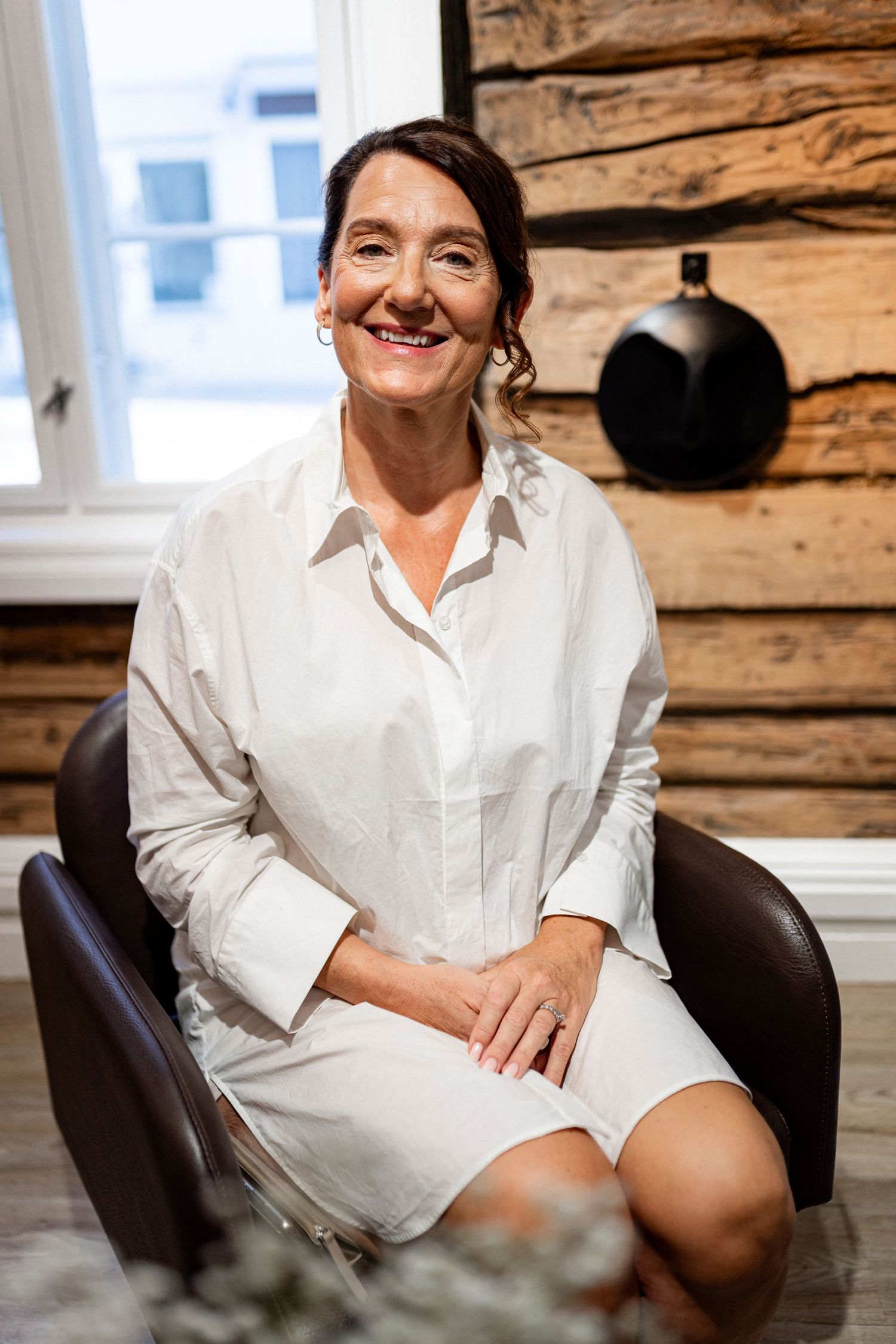 A person wearing a white shirt sits relaxed in a leather chair against a rustic wood wall.