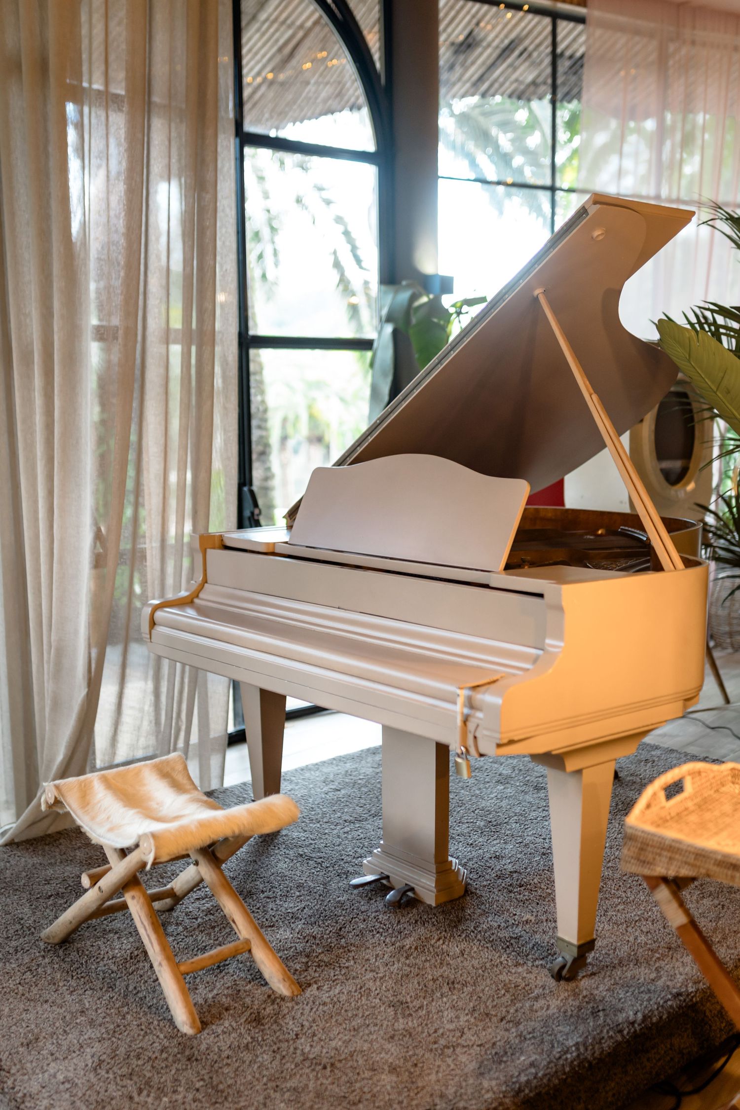 White baby grand piano near window with natural light streaming in and folding chair.