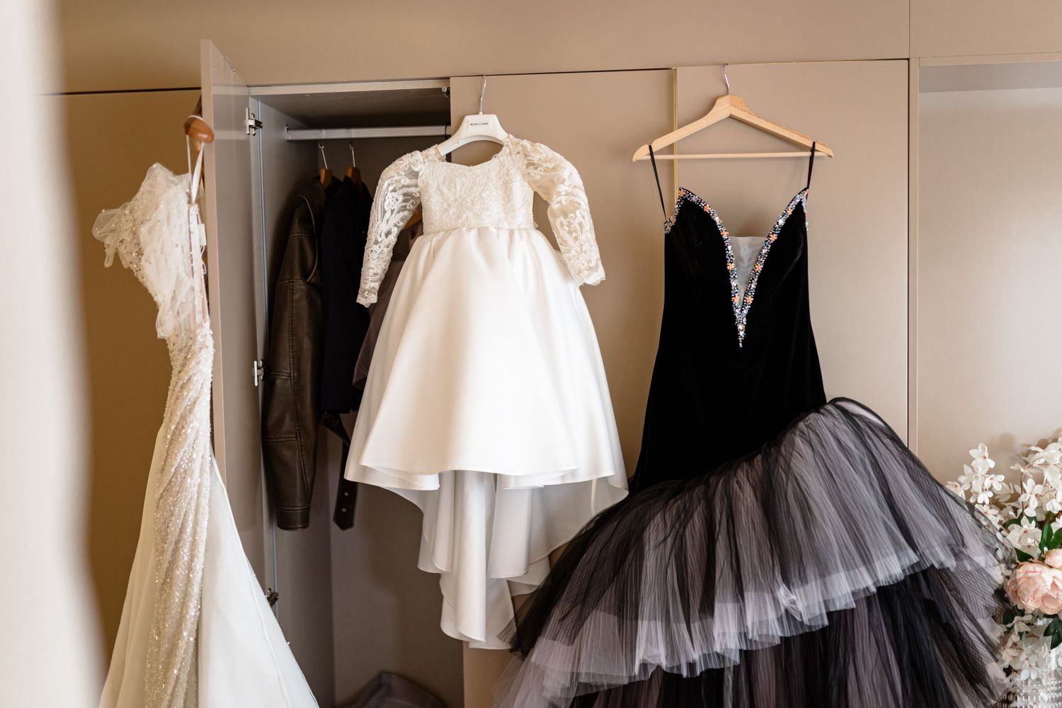 Collection of white and black formal dresses hanging on display against a beige wall.