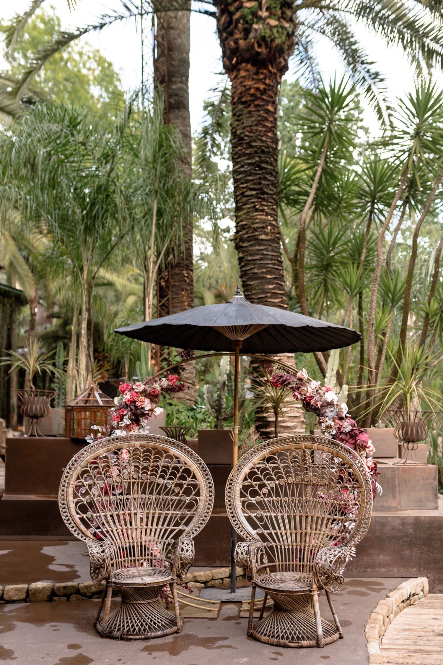 Ornate wicker peacock chairs decorated with pink flowers create a romantic outdoor seating area.
