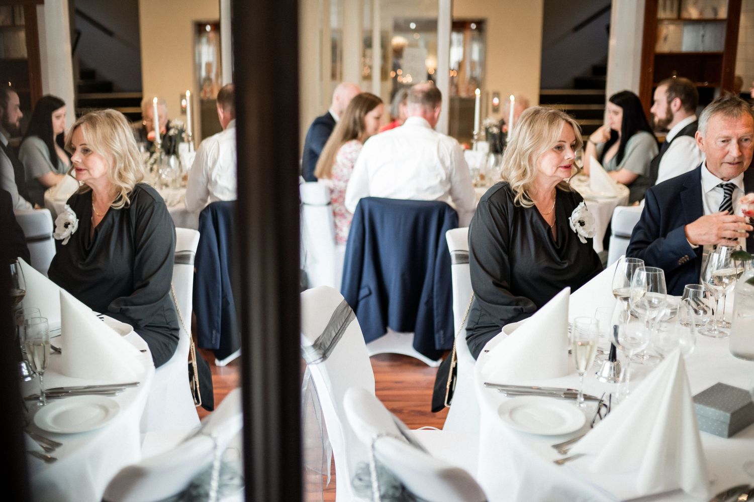 Wedding guests enjoy a formal dining experience at elegantly set tables in a reception venue.