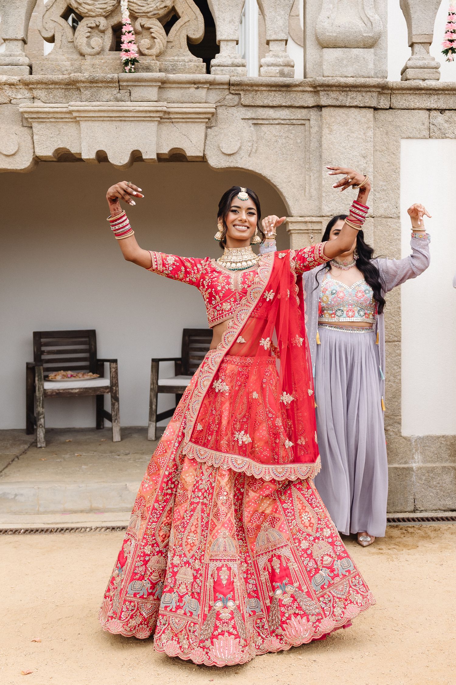 Women in red and purple traditional dresses dancing and posing in an outdoor courtyard.