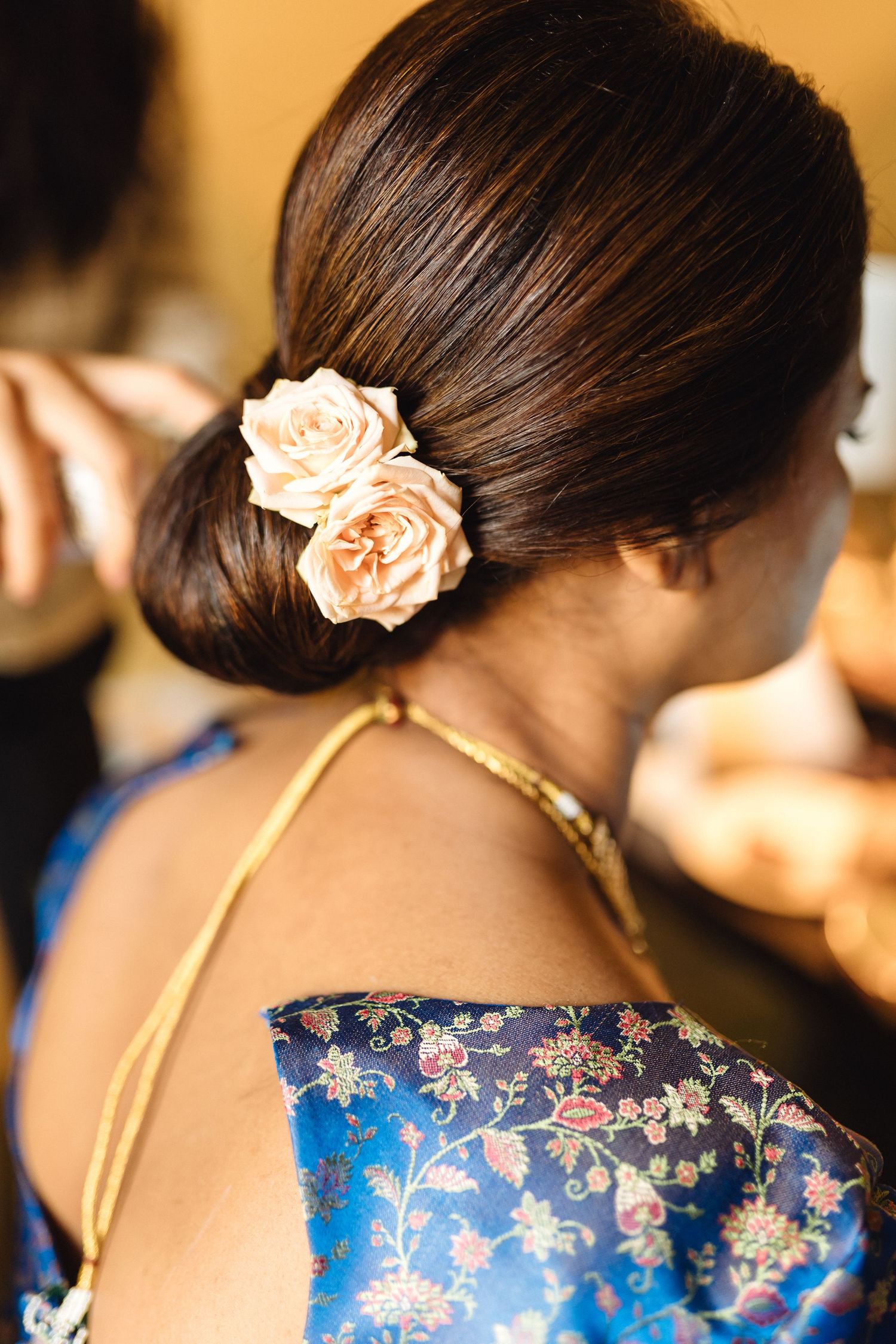 Elegant updo hairstyle with peach rose accent against blue floral fabric.