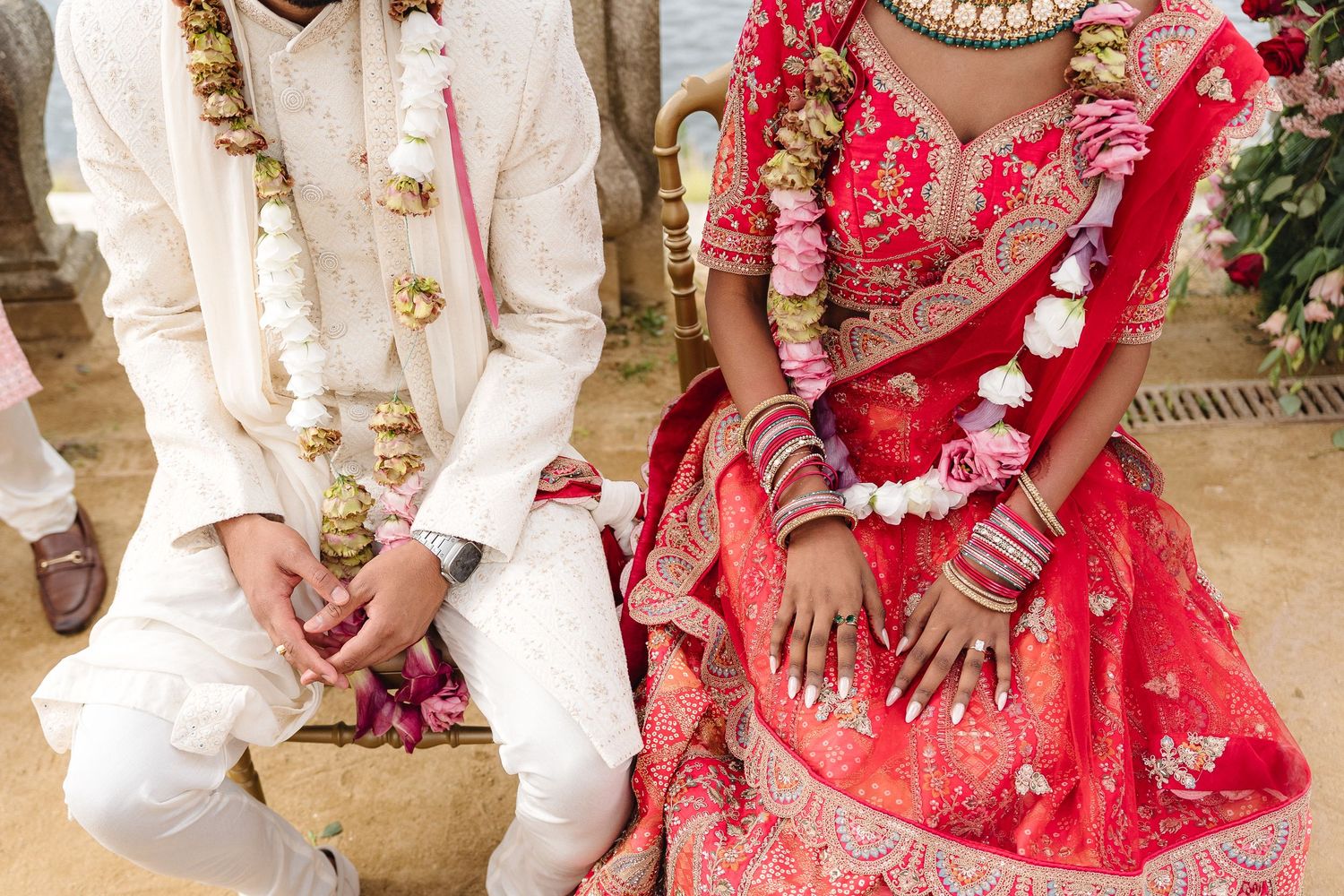Close-up of couple's hands and attire during traditional Indian wedding ceremony.