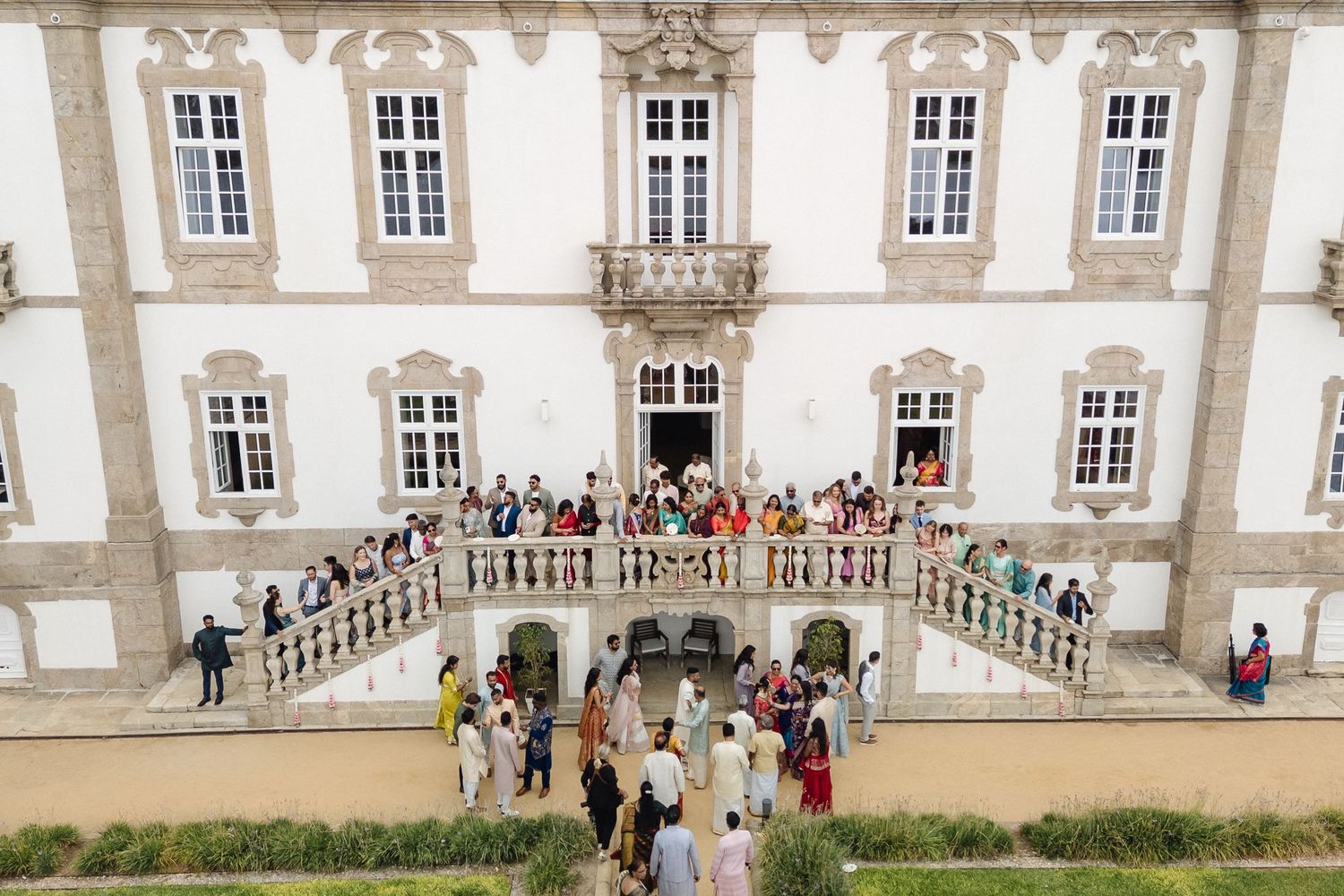 Panoramic view of a grand historic building with wedding guests gathered on its steps.