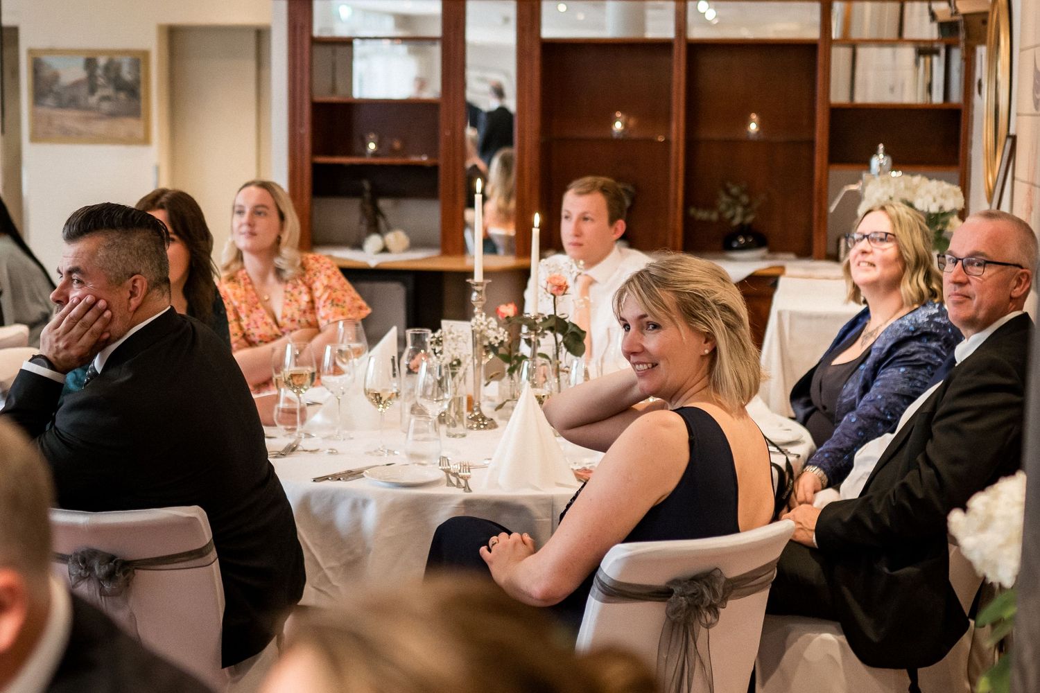 Indoor wedding reception with guests seated at formal dining tables.