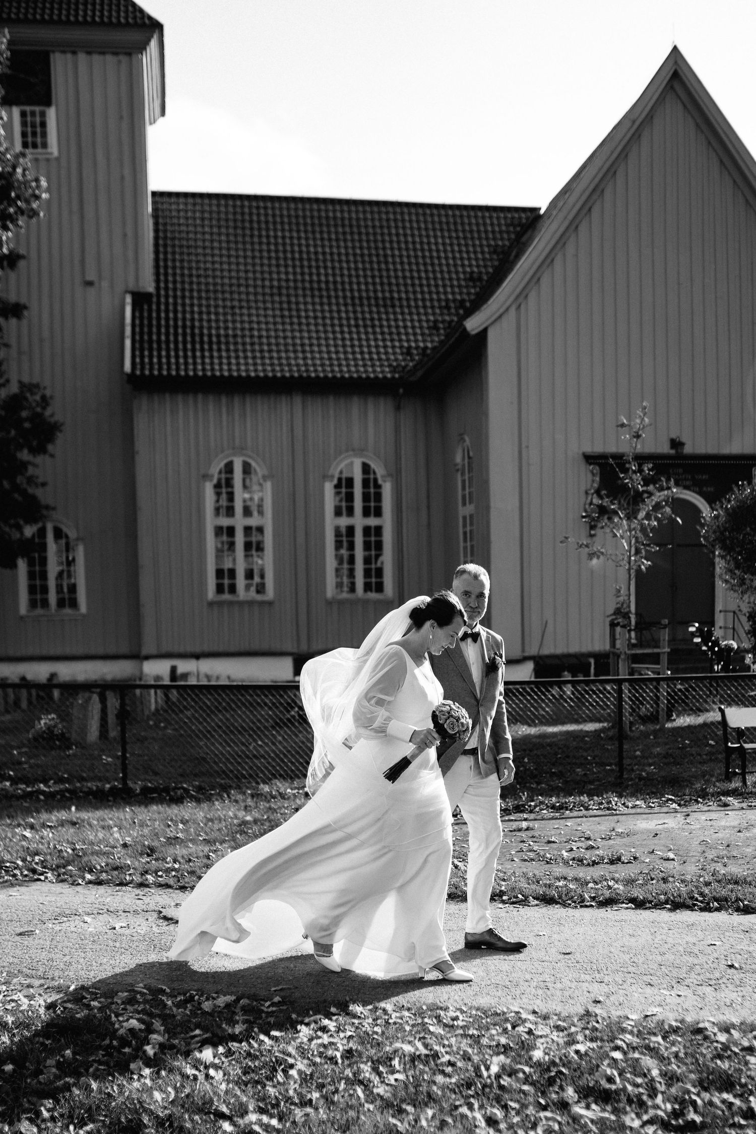 Artistic black and white sequence of a bride's dress flowing in the wind outside a church building.