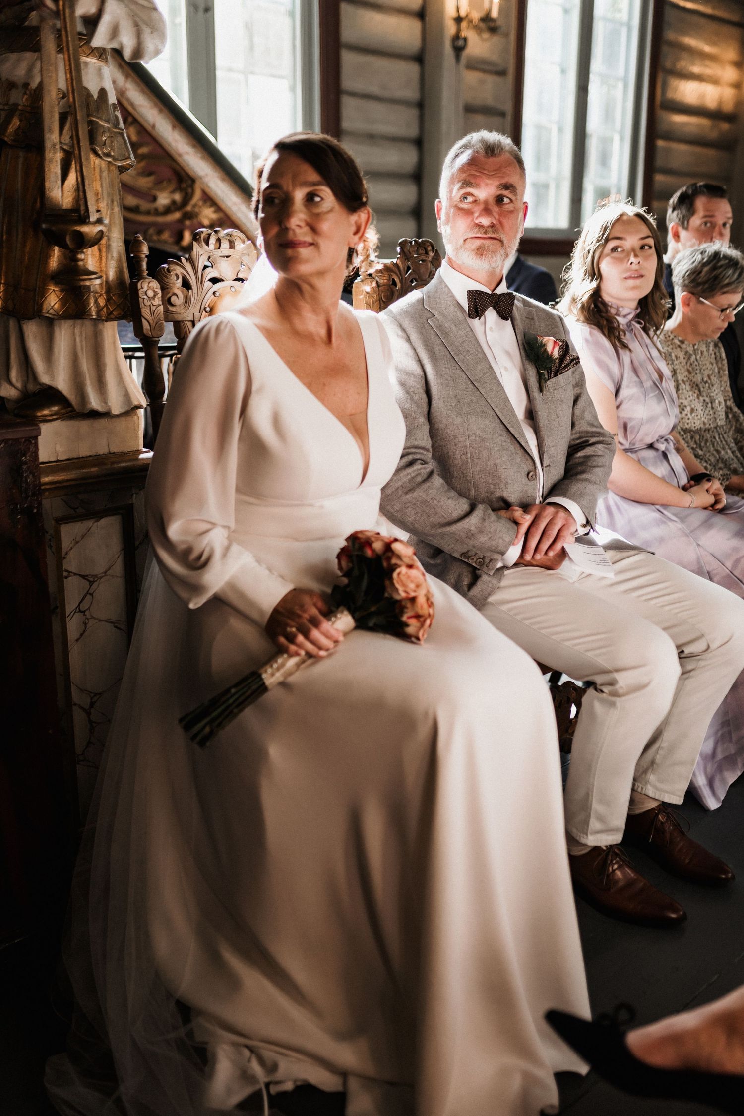 Wedding guests seated in formal attire during an indoor ceremony.