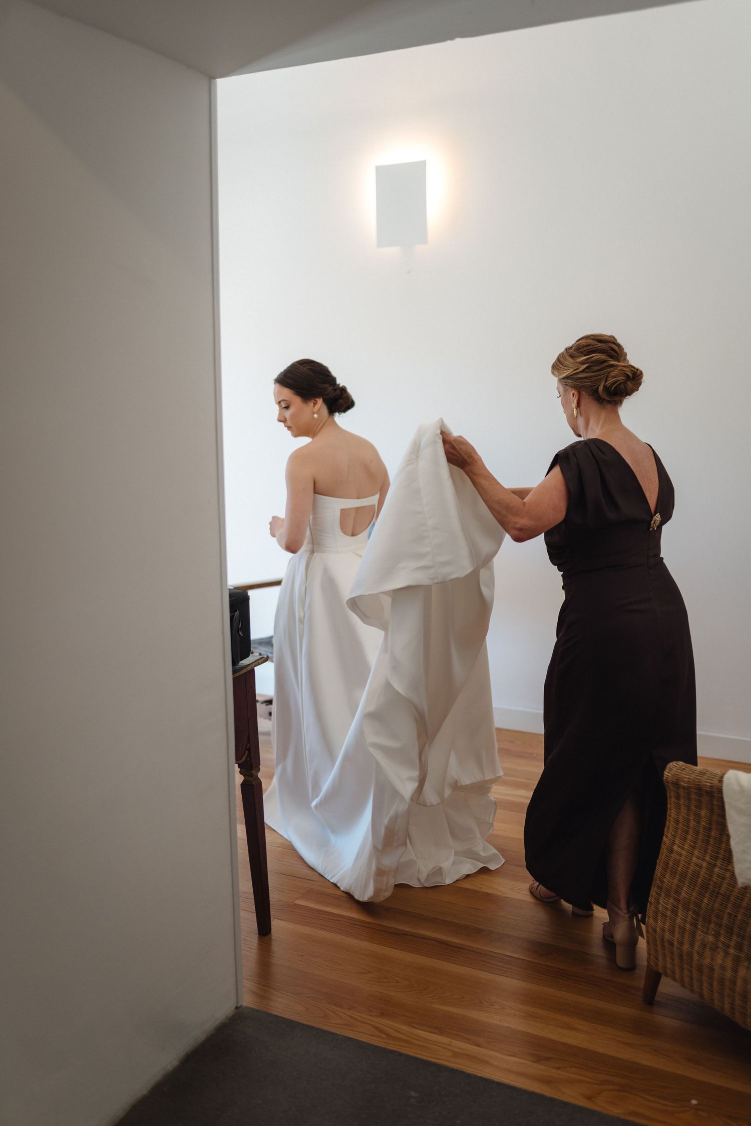 Wedding dress preparation scene with helpers in black dresses.