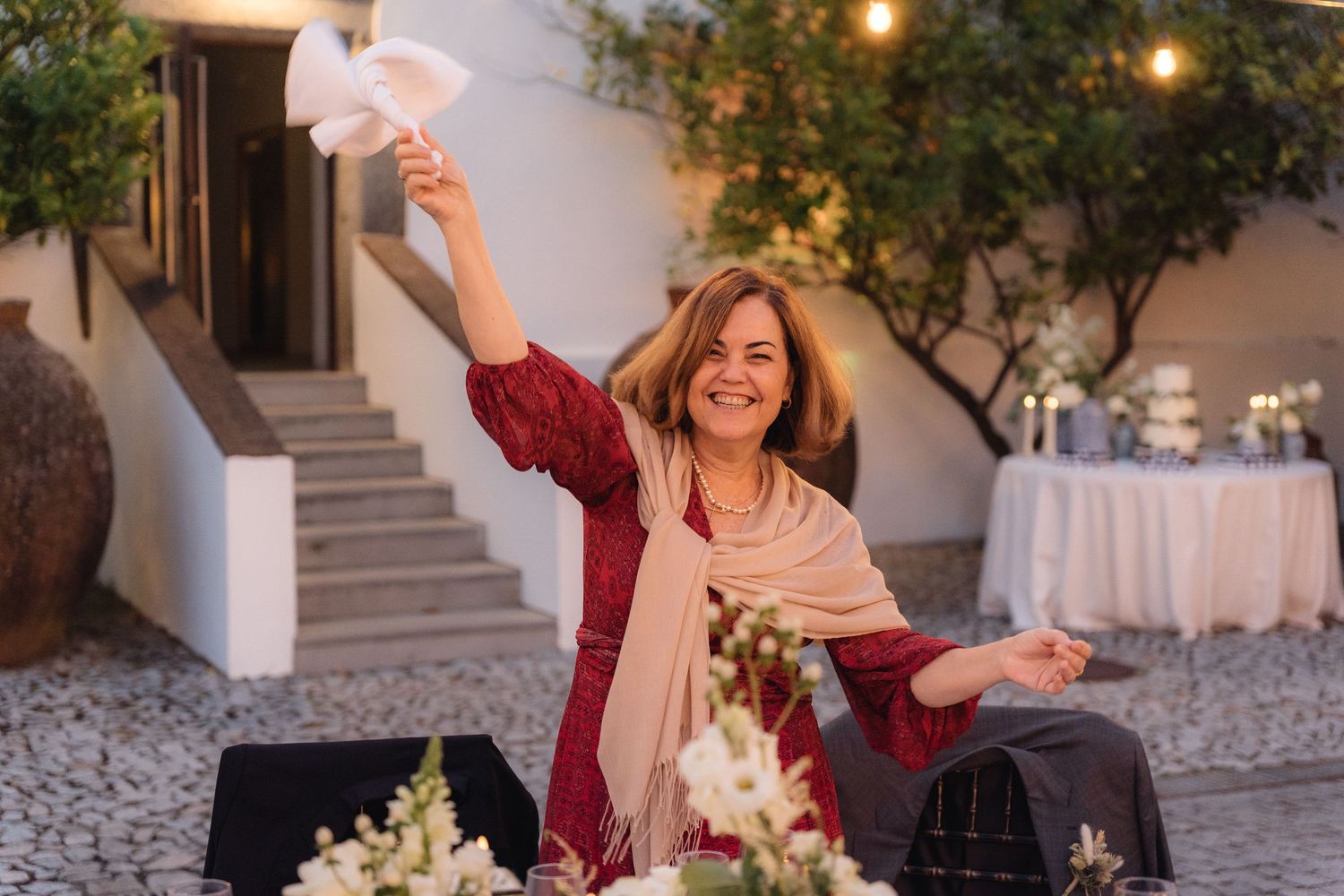 Wedding guests celebrate during outdoor reception with string lights and white decor.