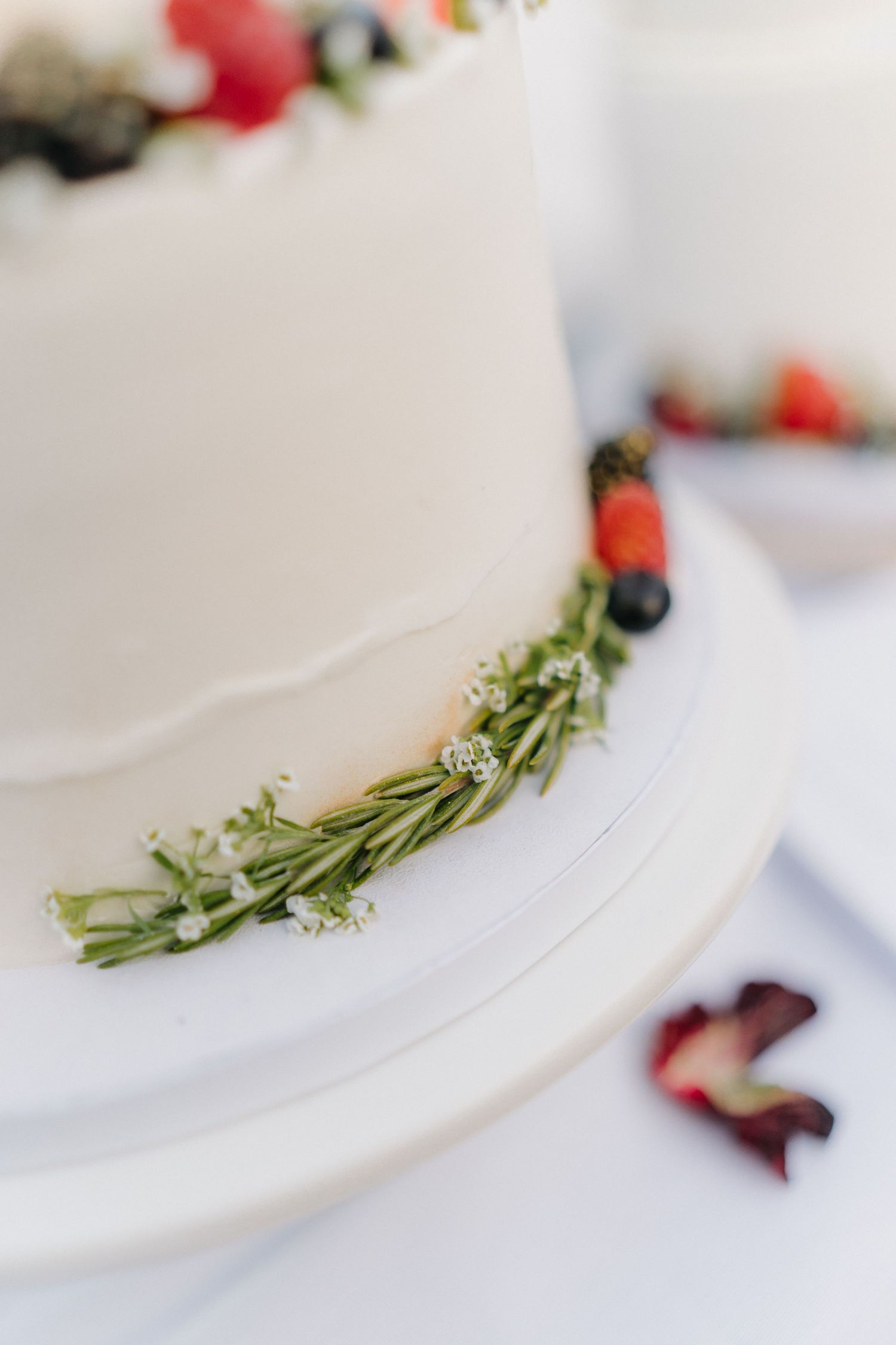 Close-up of white wedding cake decorated with fresh herbs and berries.