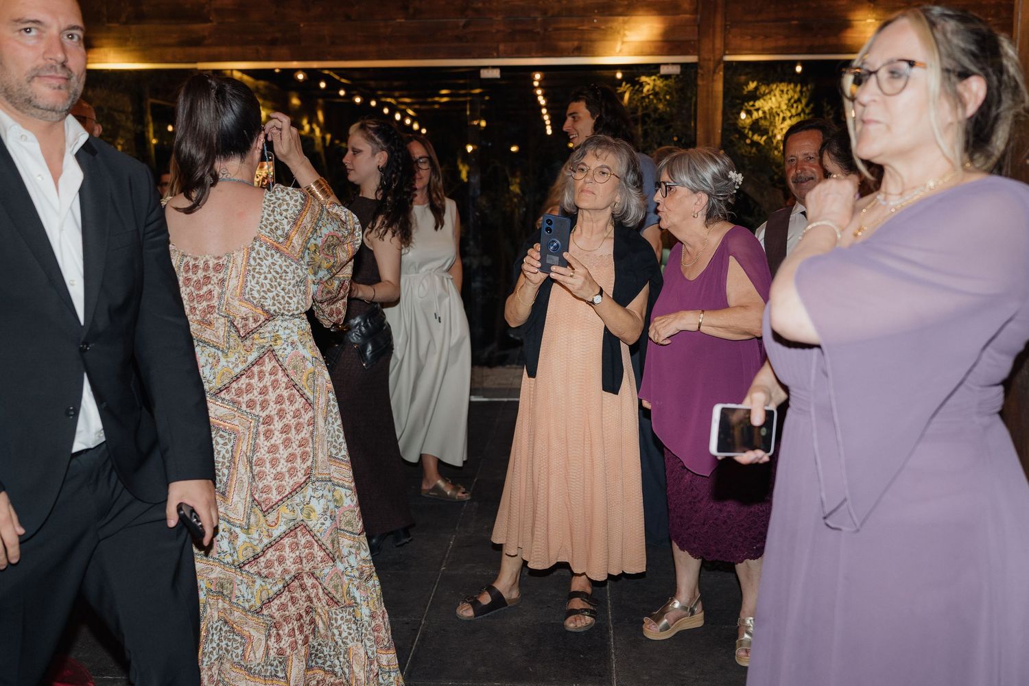 Evening wedding reception with guests dancing and mingling under decorative lighting.
