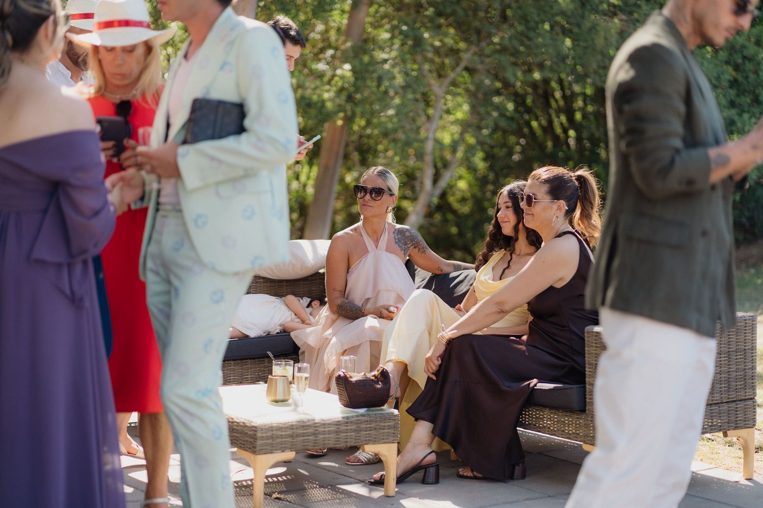 Wedding guests in formal attire relaxing and socializing at outdoor garden party.