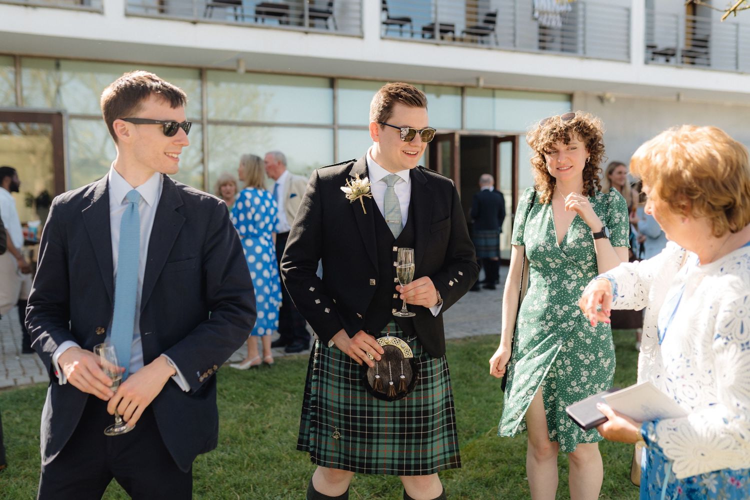 Guests in formal wear including traditional Scottish kilts socialize at an outdoor event.