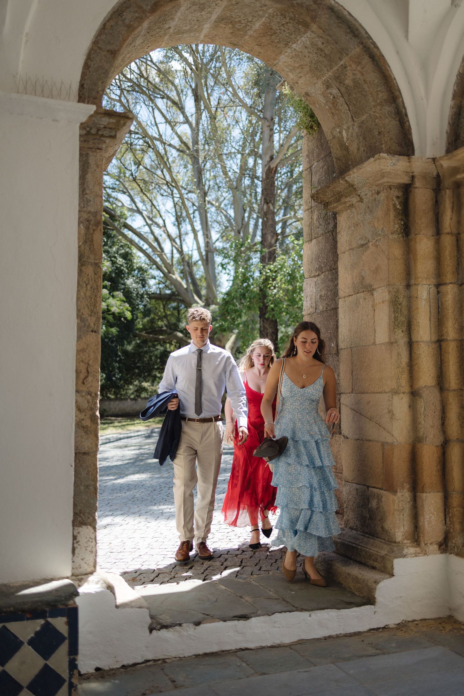 Wedding party poses under historic stone archways during outdoor celebration.