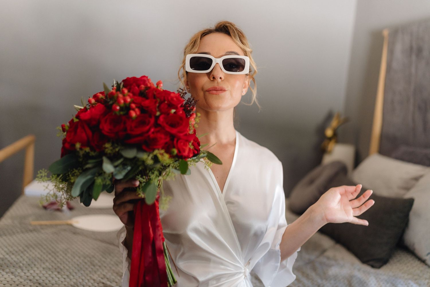 Stylish figure in white shirt and retro sunglasses holding vibrant red rose bouquet in modern interior setting.