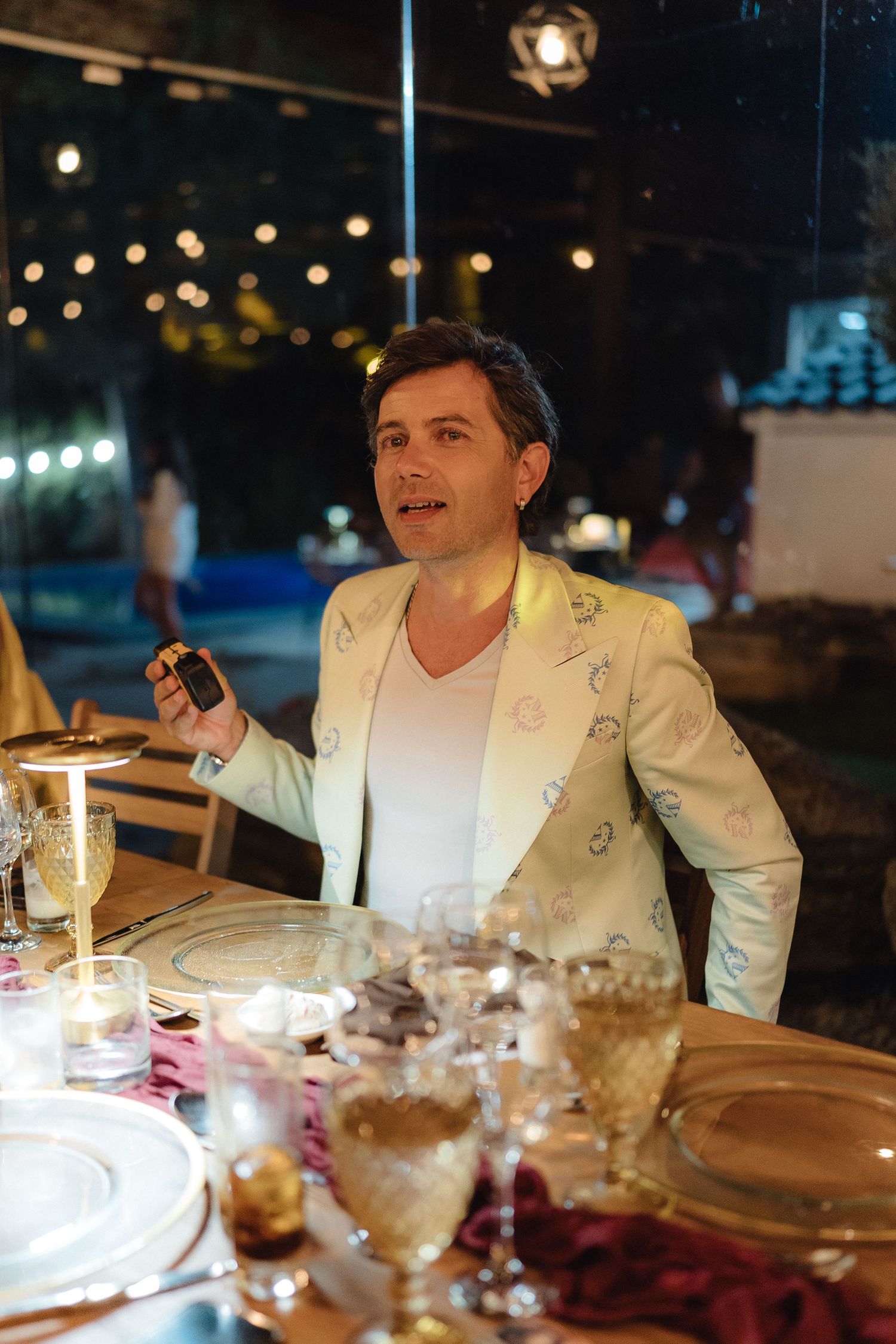 Elegant dinner table setting with guests in white jackets under ambient evening lighting.