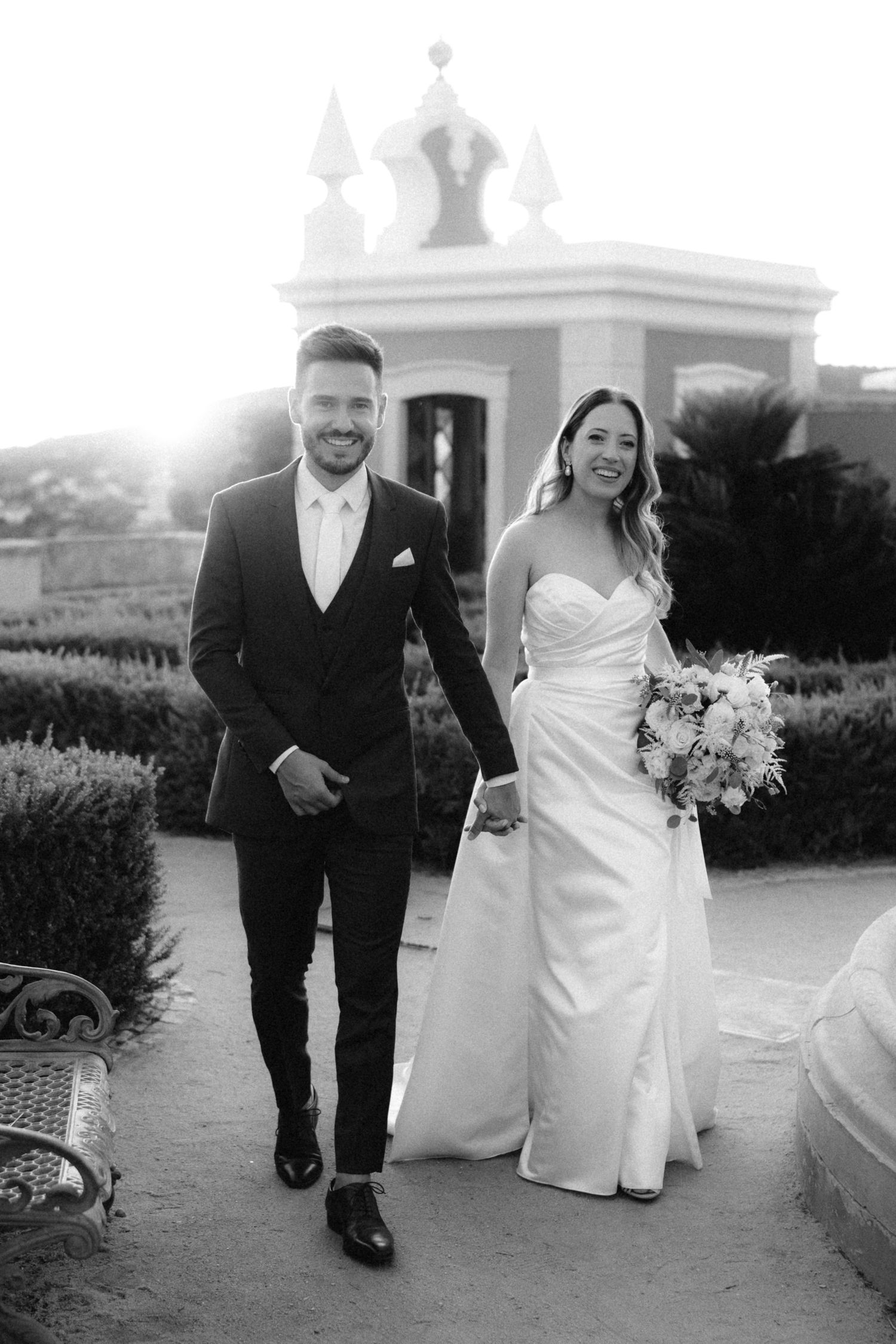 Couple strolls along garden path with pink architectural details and sunset lighting.