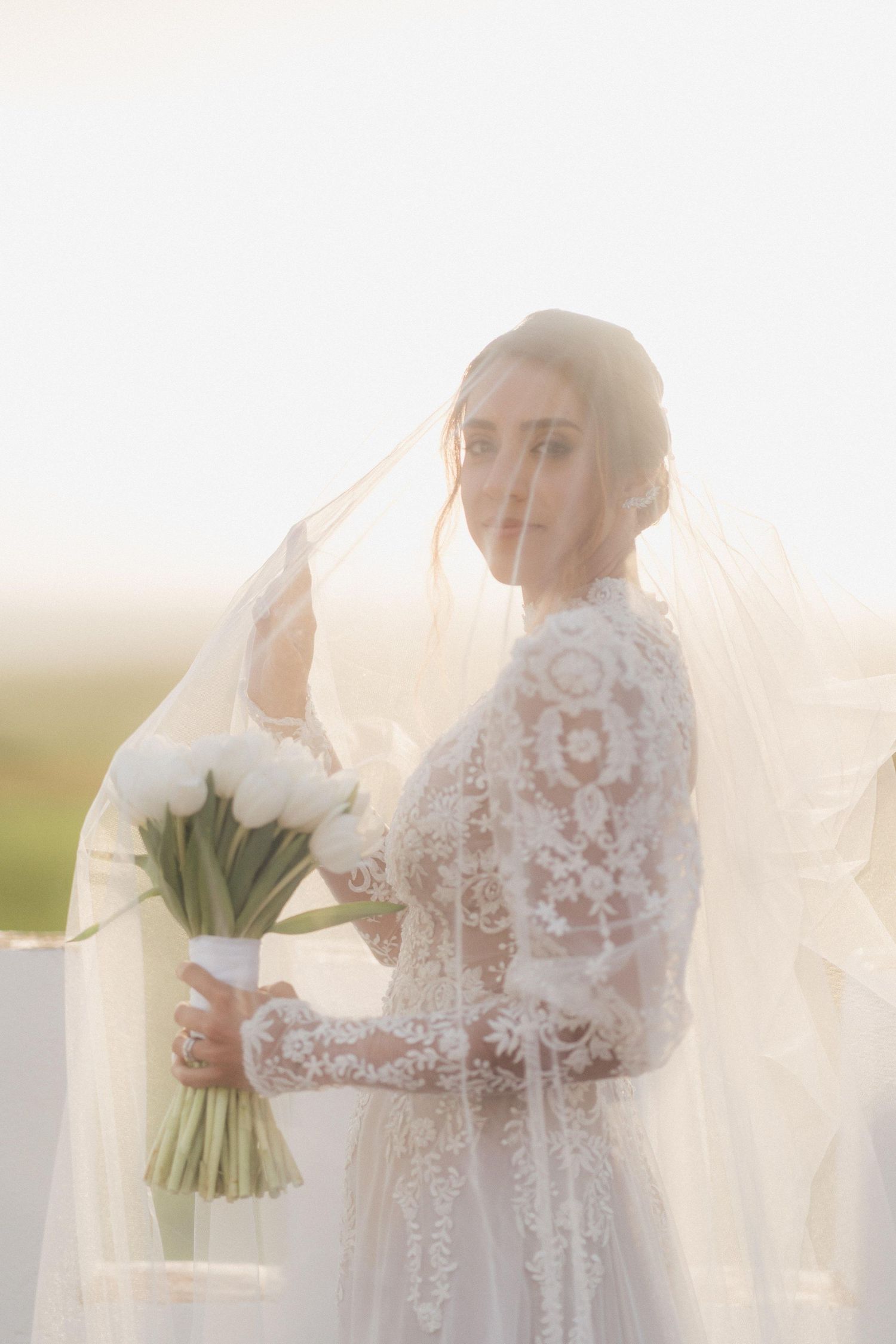 Ethereal bridal portrait with sunlit veil and white bouquet creating a dreamy atmosphere.