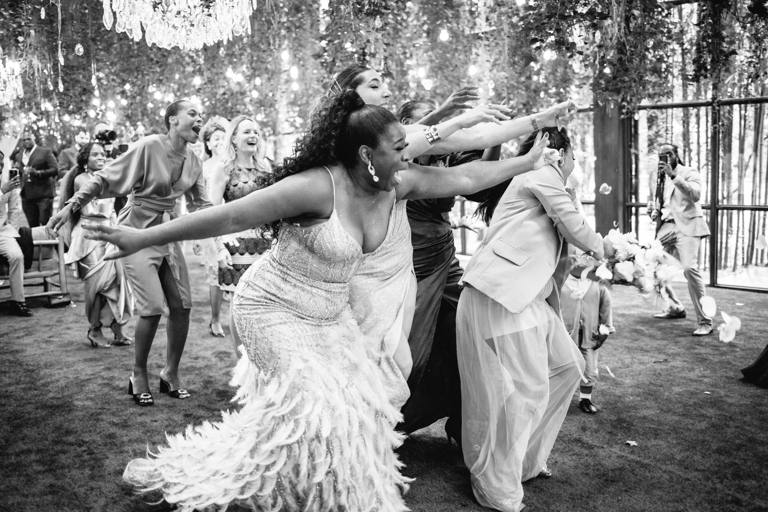 A black and white photo of wedding guests dancing and celebrating at a reception.