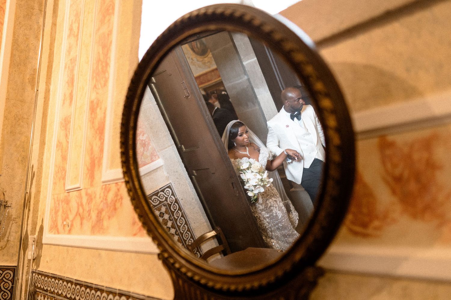 A wedding moment reflected in an ornate circular mirror mounted on a wooden wall.