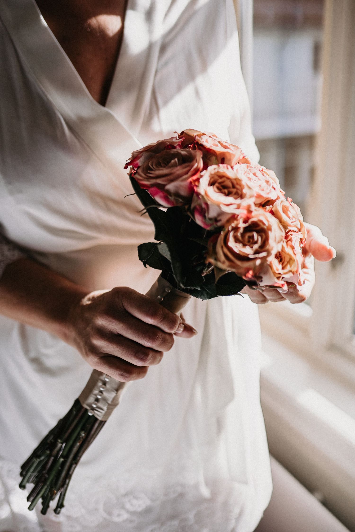 Close-up of hands holding a delicate bouquet of pink roses against a white dress.
