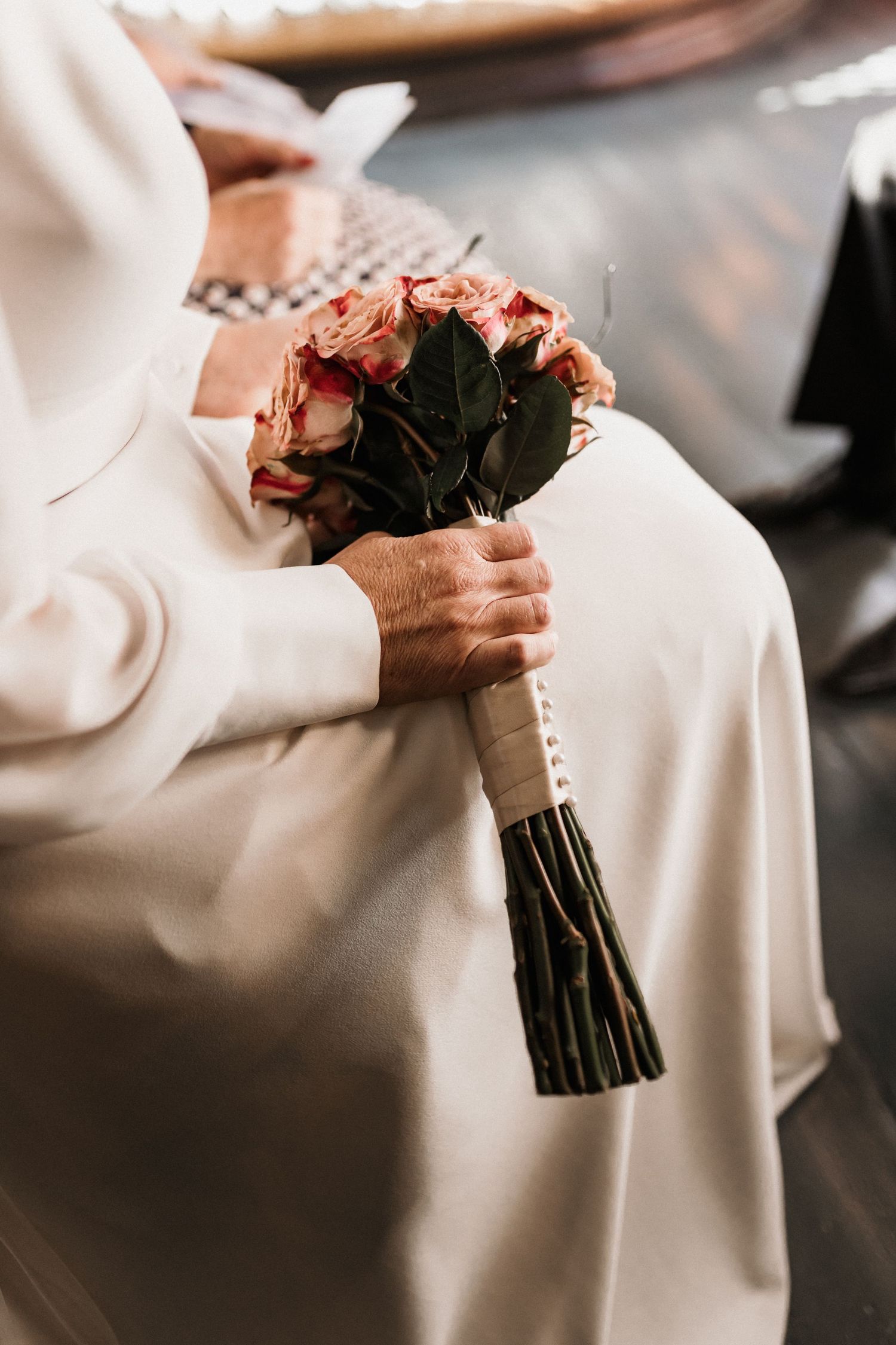 Close-up shots of hands holding a pink rose bouquet against a white wedding dress.